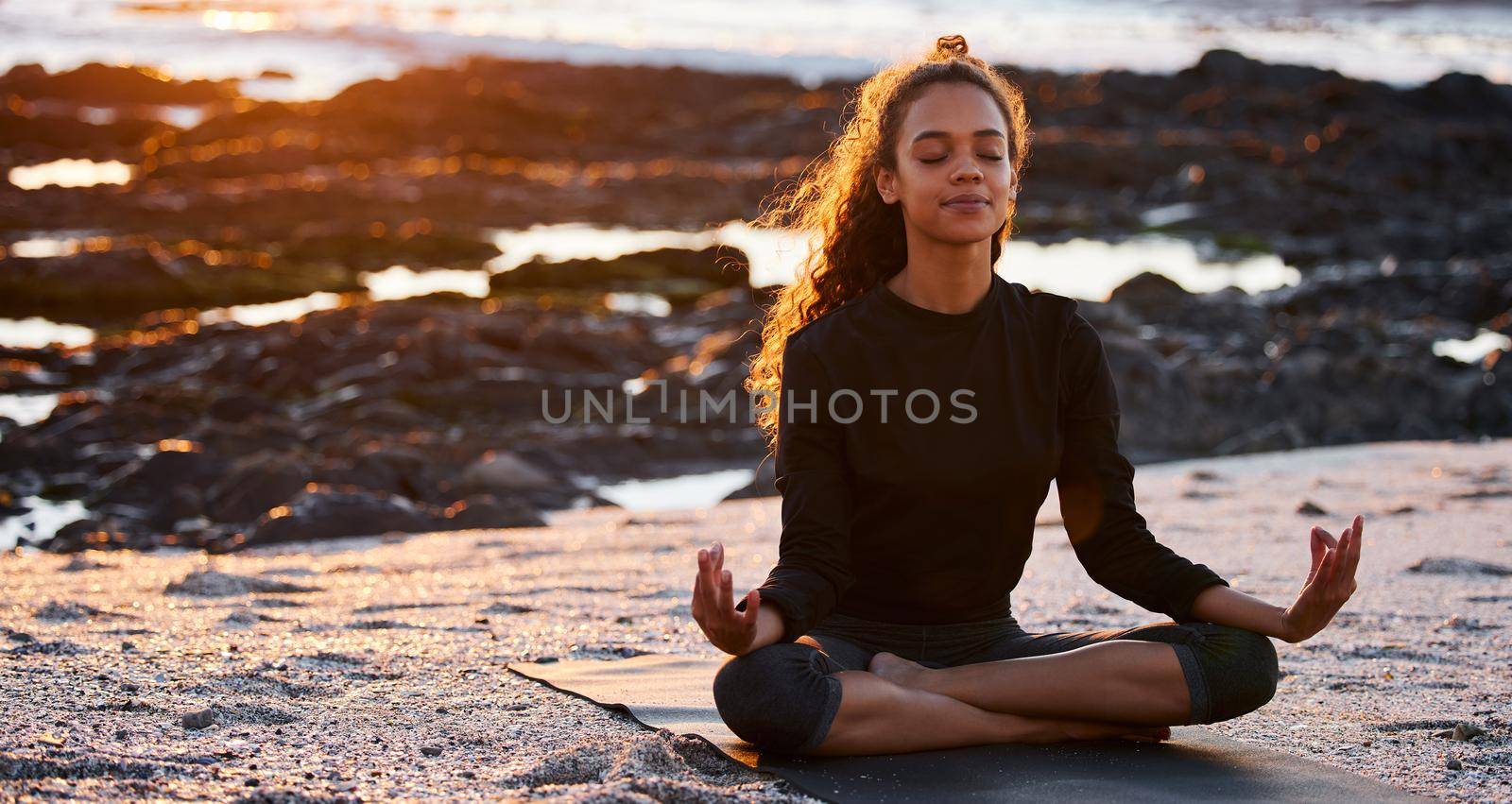 Gratitude brings positive change. an attractive young woman sitting alone on a mat and meditating on the beach at sunset. by YuriArcurs