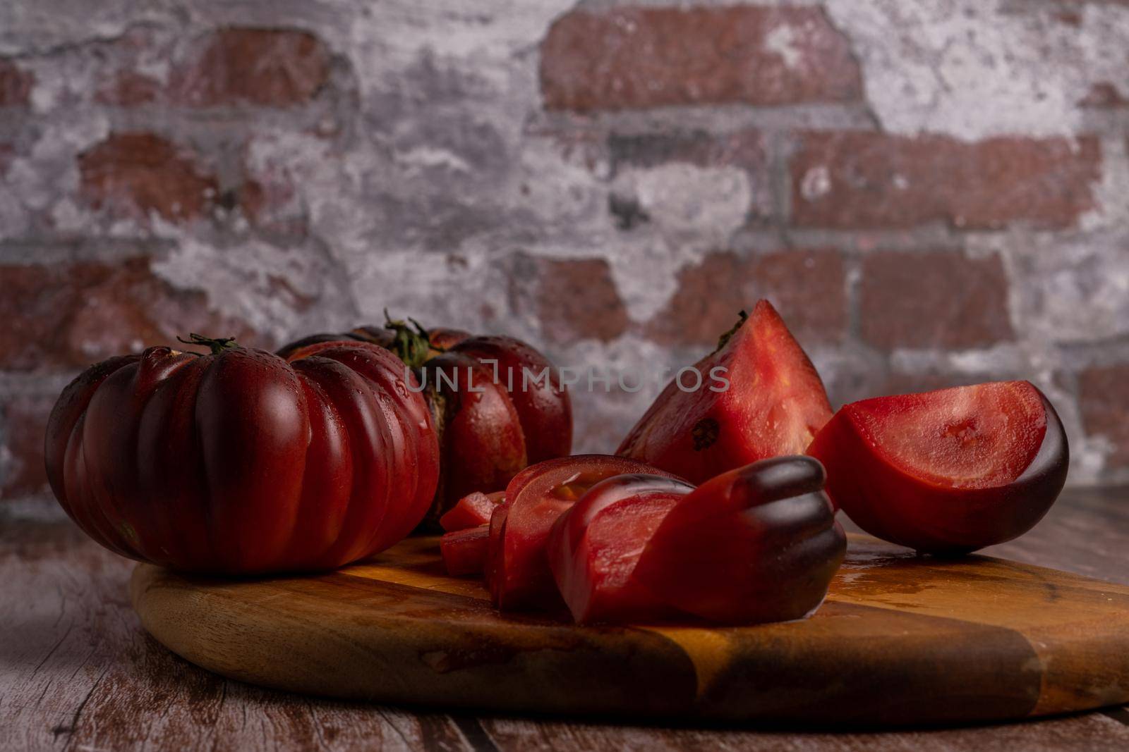 group of cut and whole organic Moorish tomatoes on a wooden board with a brick wall in the background