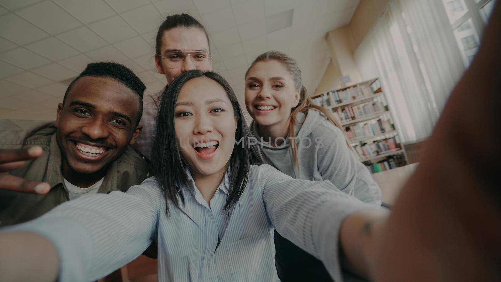 Point of view of asian girl holding smartphone taking selfie photos with cheerful classmates and have fun at university library by silverkblack