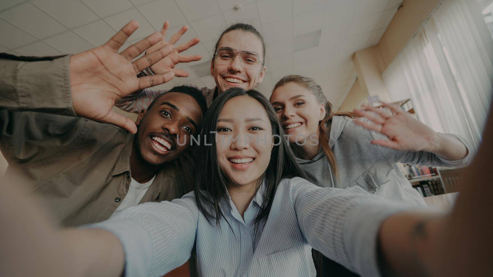 Point of view of asian girl holding smartphone taking selfie photos with cheerful classmates and have fun at university library indoors