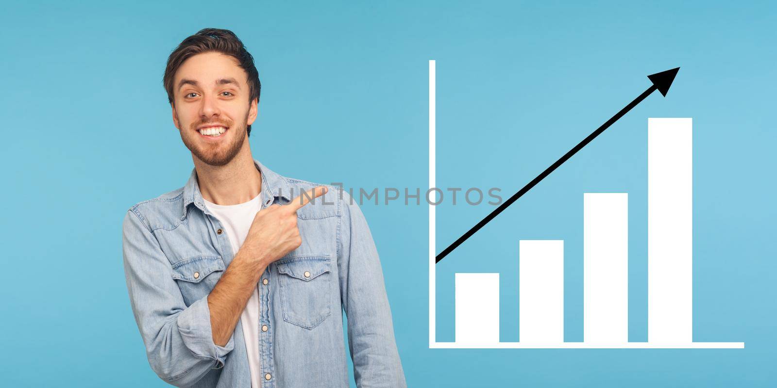 Portrait of happy joyful young bearded man standing, pointing aside and showing business growth graph. indoor studio shot isolated on blue background