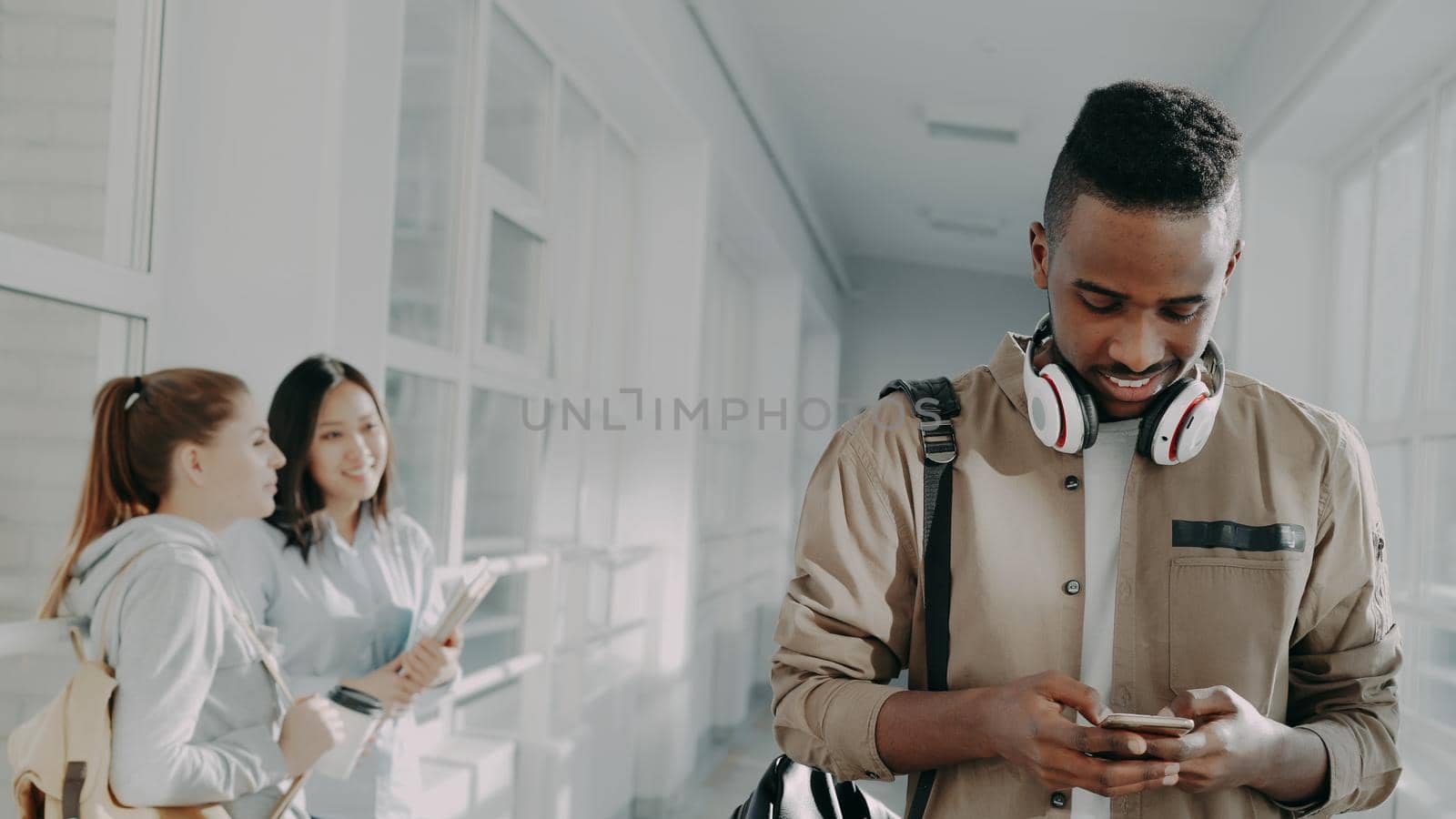 Handsome student walking thoughtfully down corridor in univrsity holding phone smiling by silverkblack