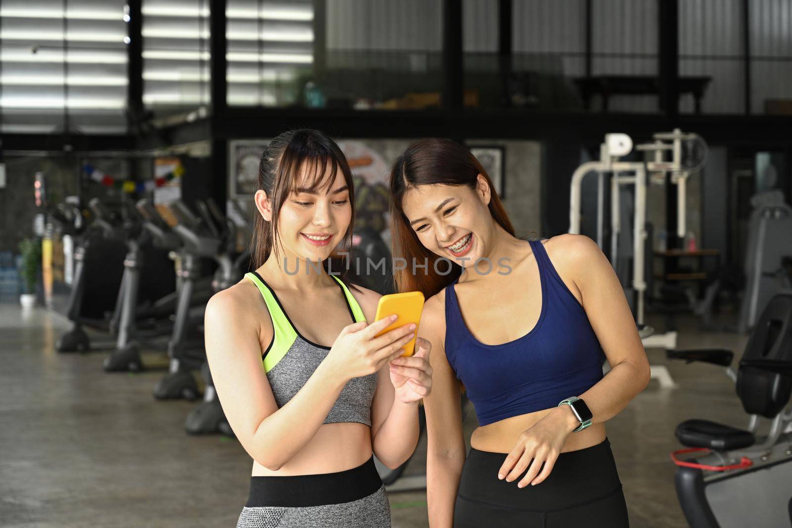 Two asian women in sportswear and using smart phone in the gym.