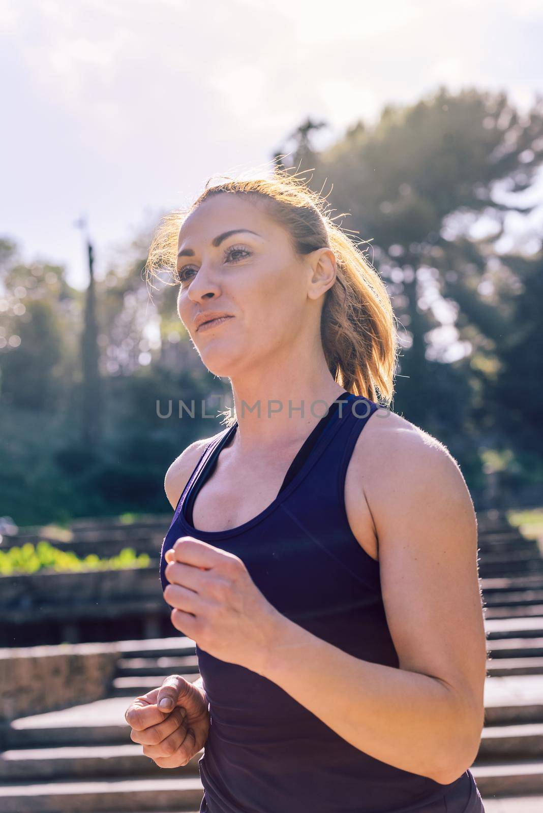 vertical portrait of young sports woman jogging during outdoor workout at the park at the morning with sunlight, sport and healthy lifestyle concept