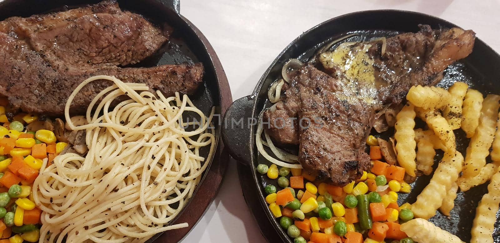The best food in the world beef steak along with fried potatoes with delicious mushroom sauce and salad and spaghetti plated in beautiful black plate