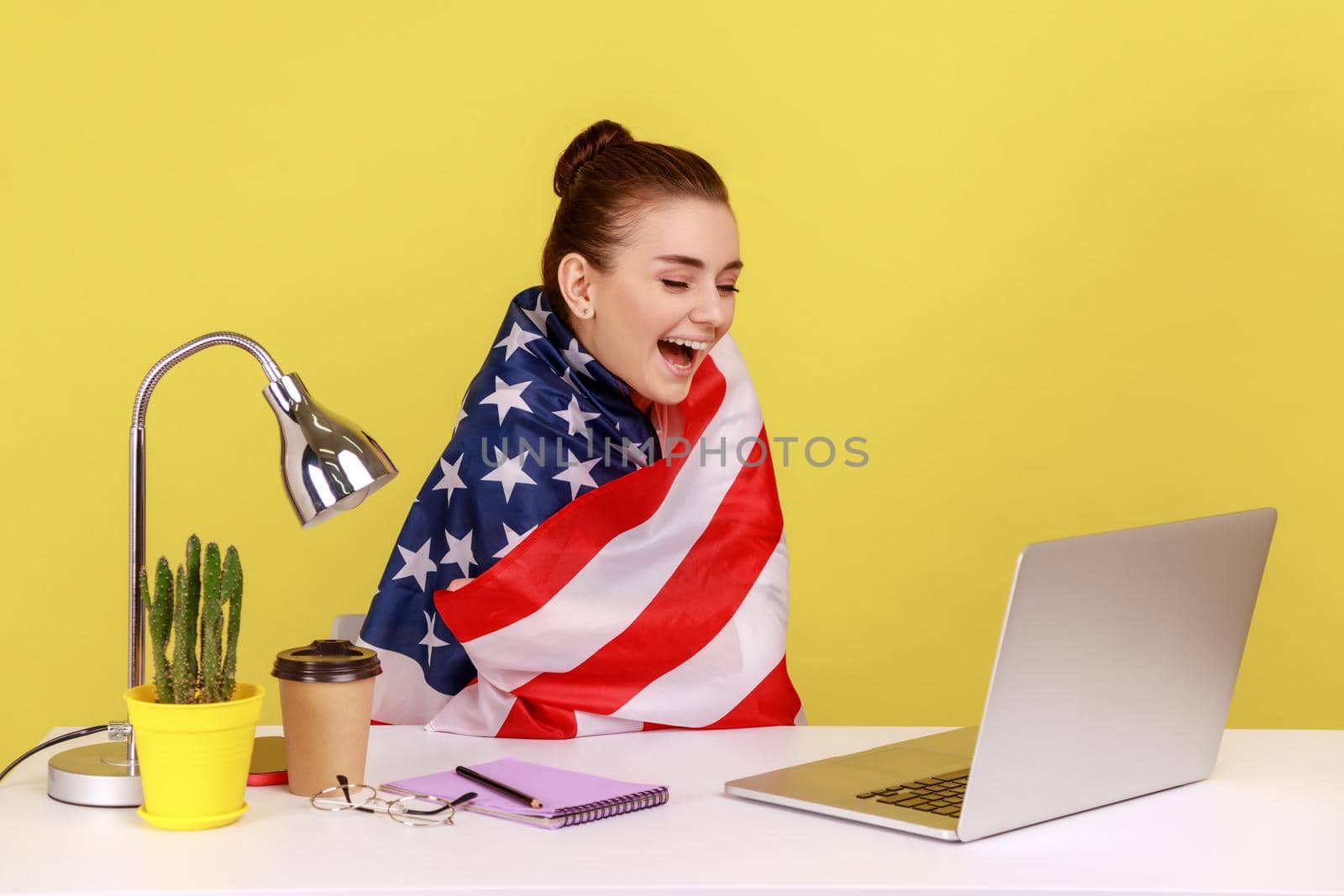 Happy woman employee sitting wrapped in USA flag, shouting for joy in office workplace. by Khosro1