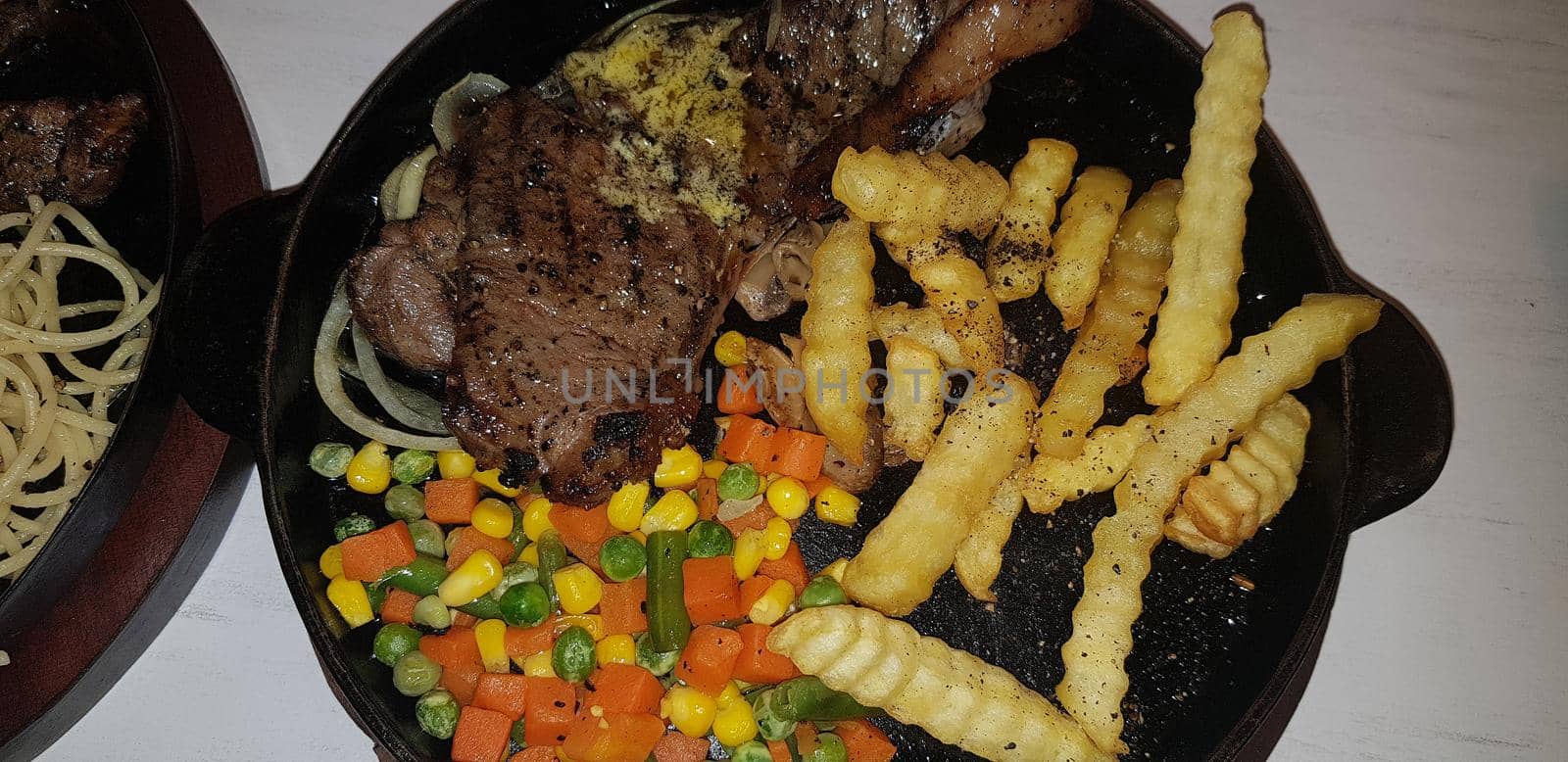 The best food in the world beef steak along with fried potatoes with delicious mushroom sauce and salad and spaghetti plated in beautiful black plate