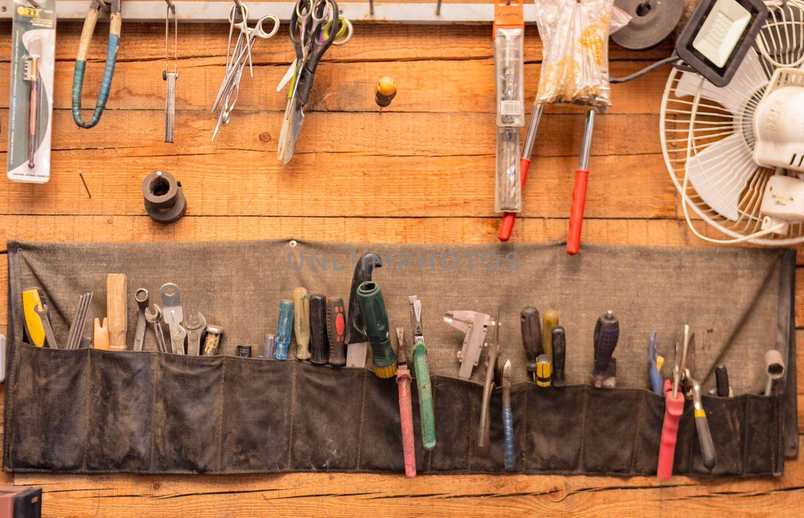 Old different tools in hanging canvas organizational wall mounted hardware storage with pockets in garage, selective focus