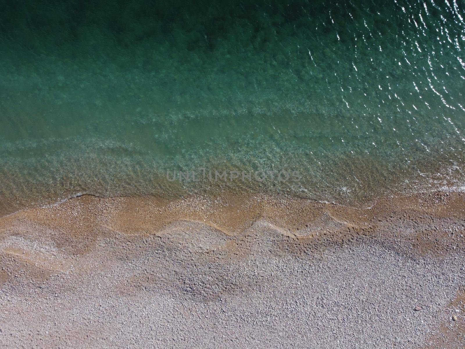 Aerial view from above on azure sea and pink pebbles beach. Small waves on cristal clear water surface in motion blur. Summer ocean sea beach background. Nobody. Holiday, vacation and travel concept by panophotograph