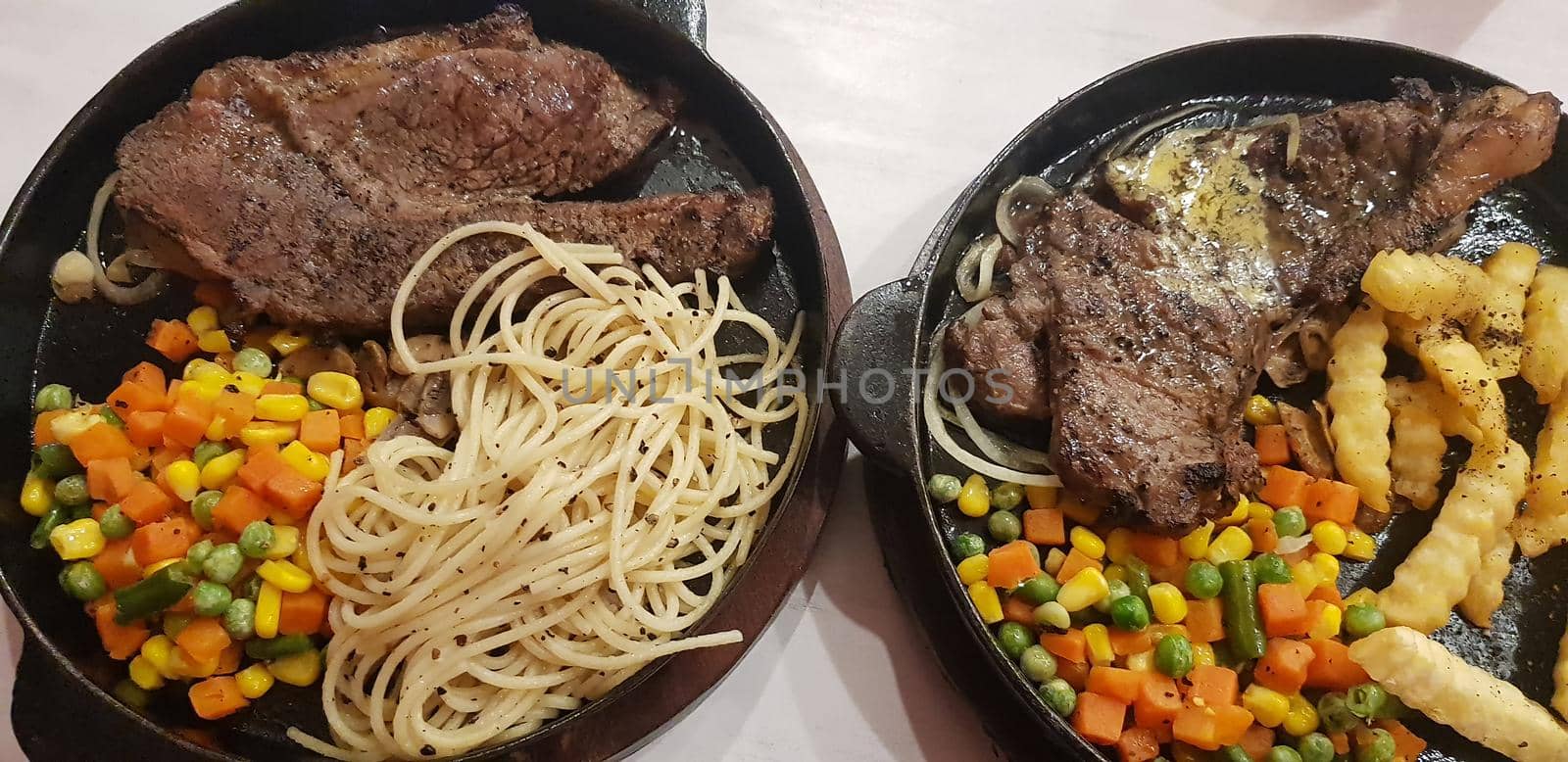 The best food in the world beef steak along with fried potatoes with delicious mushroom sauce and salad and spaghetti plated in beautiful black plate
