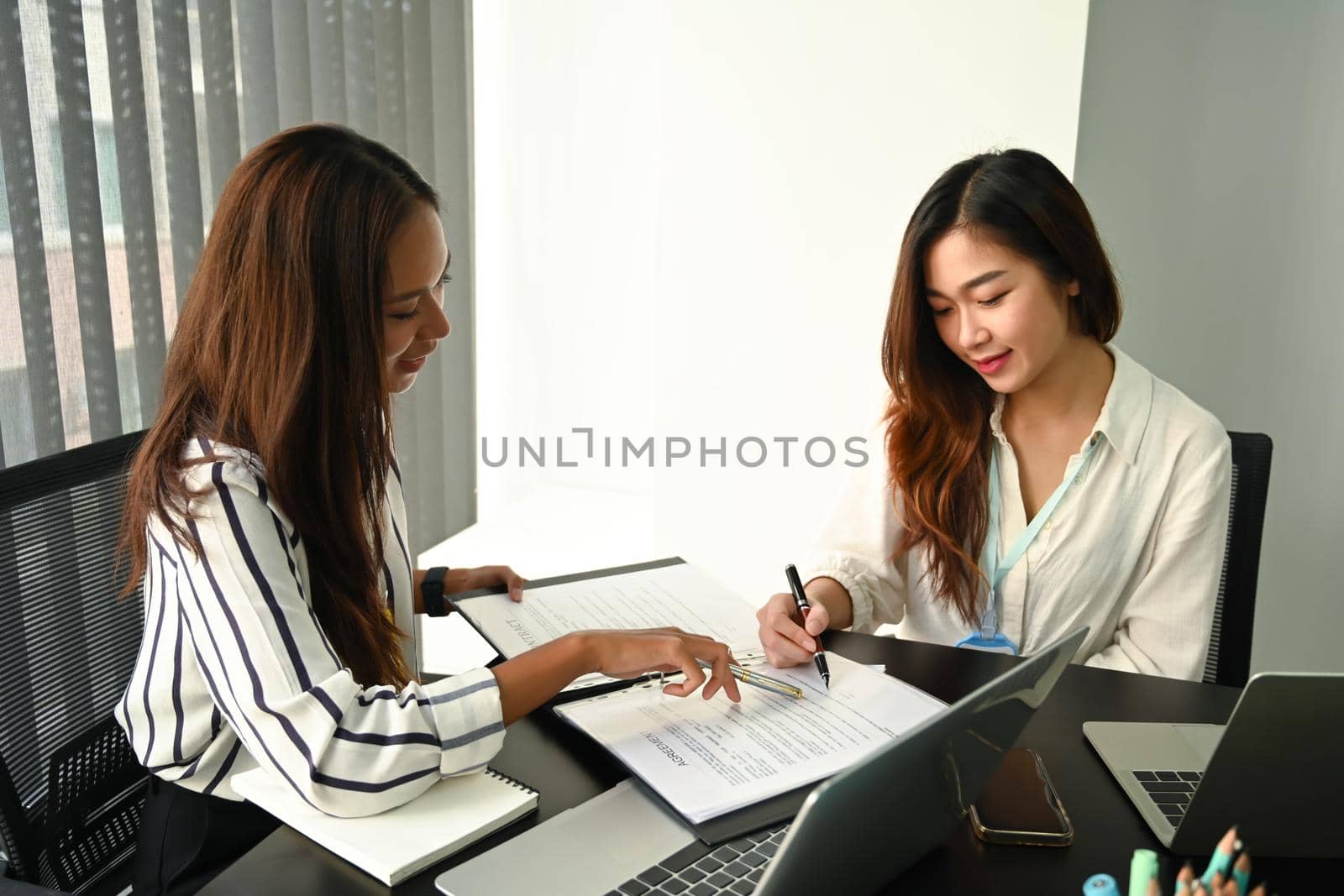 Two businesswomen discussing project strategy together at office. by prathanchorruangsak