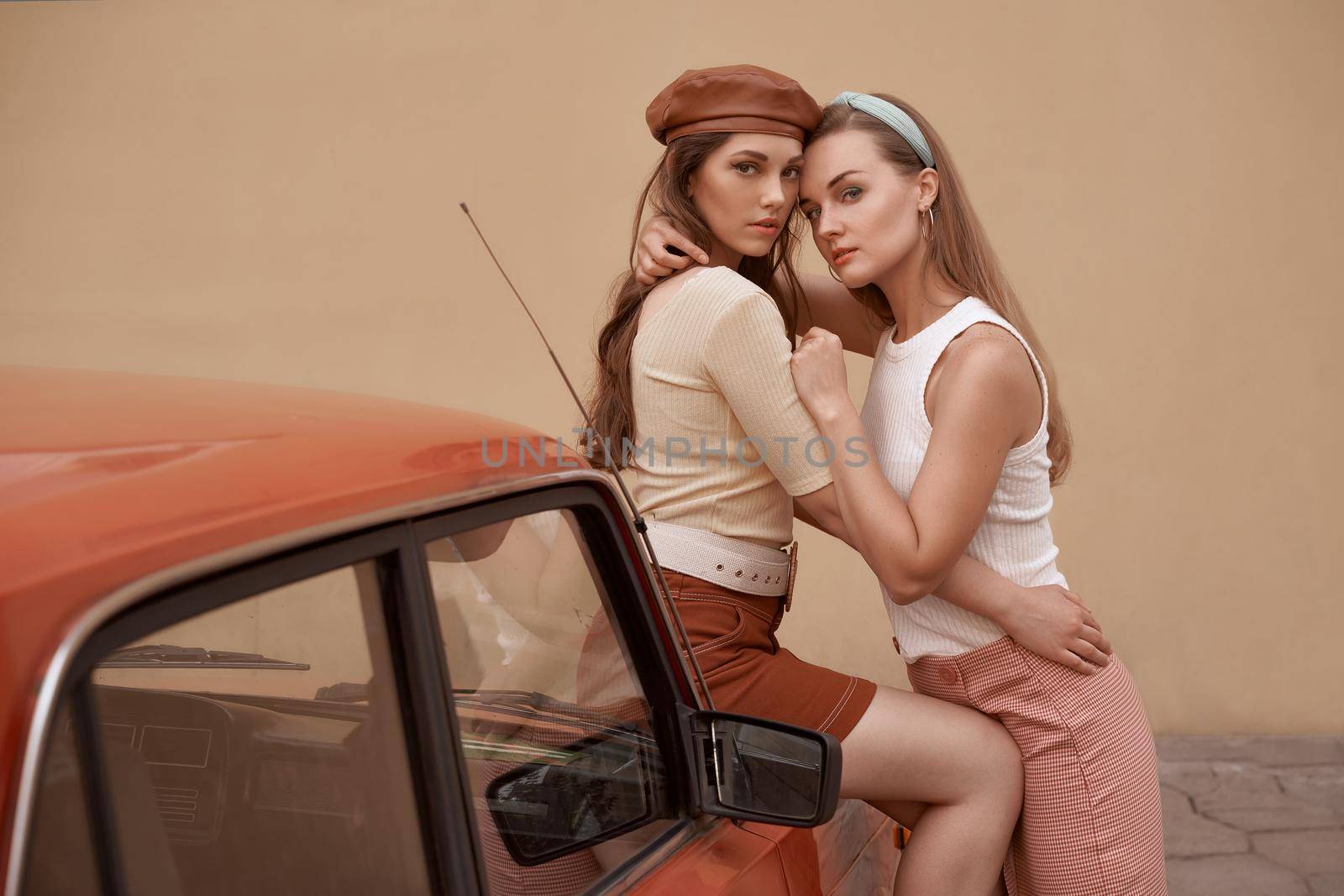 Young beautiful girls dressed in retro vintage style enjoying the old european city summertime lifestyle. Women posing by an old car.