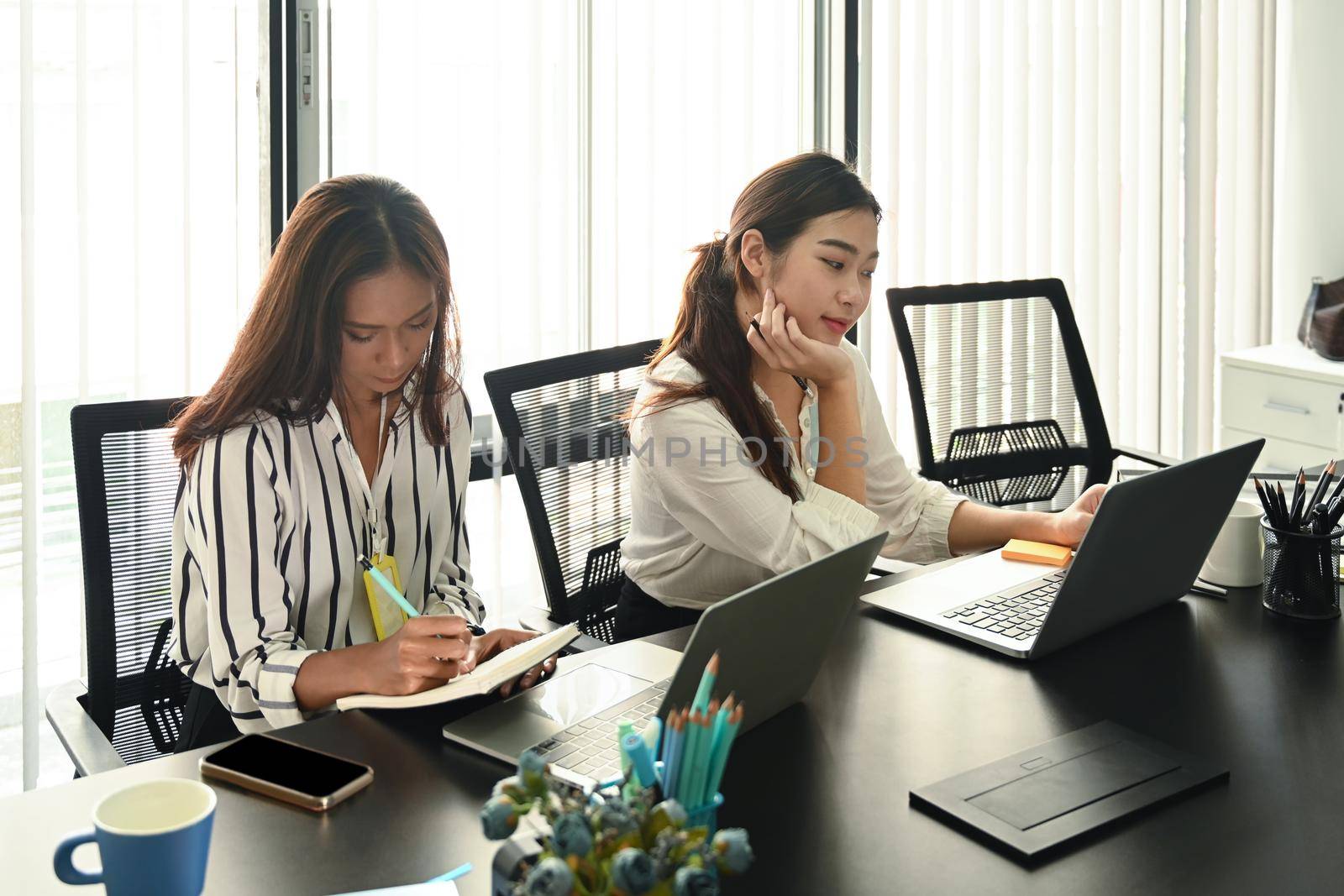 Two business colleagues working in modern workplace. by prathanchorruangsak