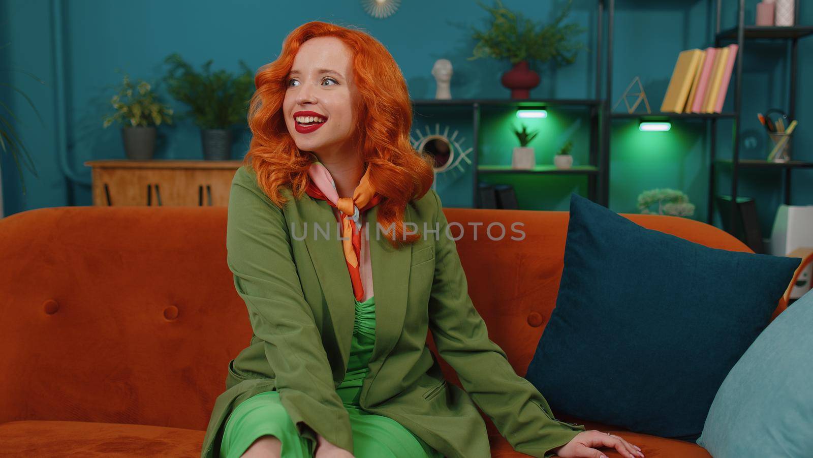 Portrait of beautiful happy calm young caucasian redhead girl smiling friendly, glad expression looking away dreaming resting, relaxation feel satisfied concept good news sitting on sofa at home room