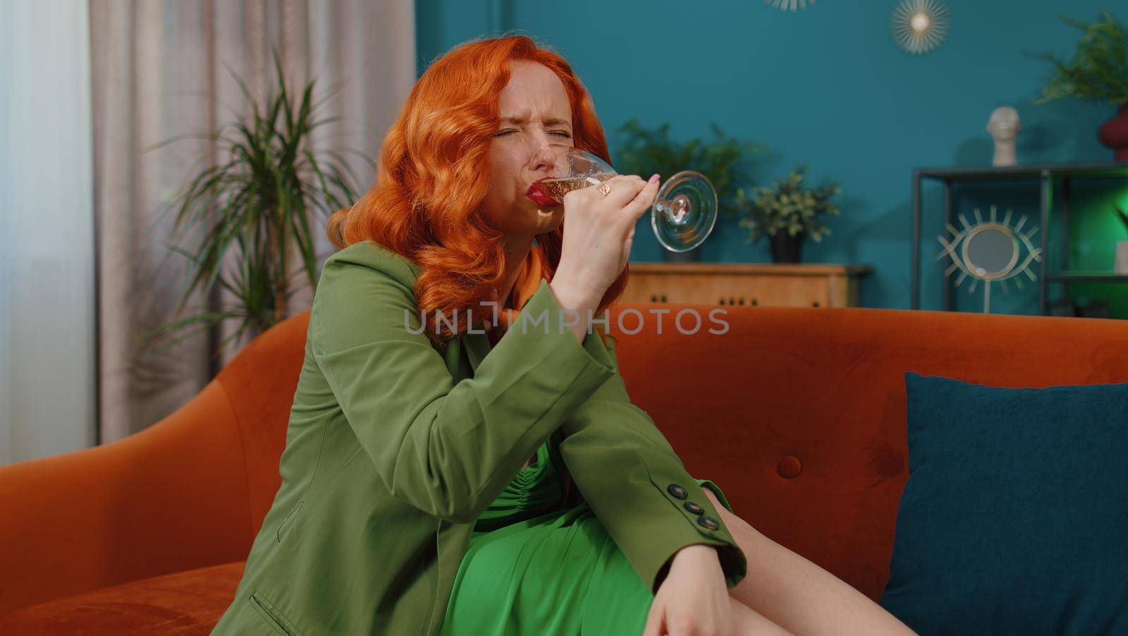 Sad young redhead woman sitting at home looks pensive of unrequited love, suffers from unfair situation, drinking champagne. Girl problems, break up, depressed feeling bad annoyed, burnout, bankruptcy