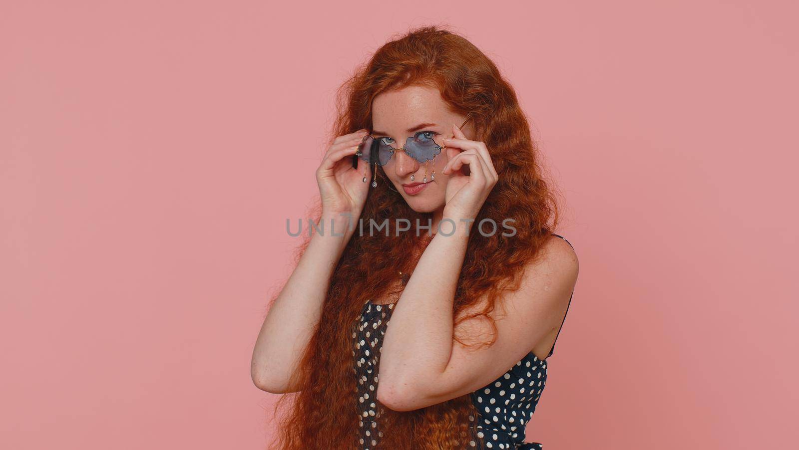 Portrait of seductive cheerful stylish woman in dress wearing sunglasses, charming smile. People emotions concept. Young lovely redhead ginger freckles girl isolated alone on pink studio background