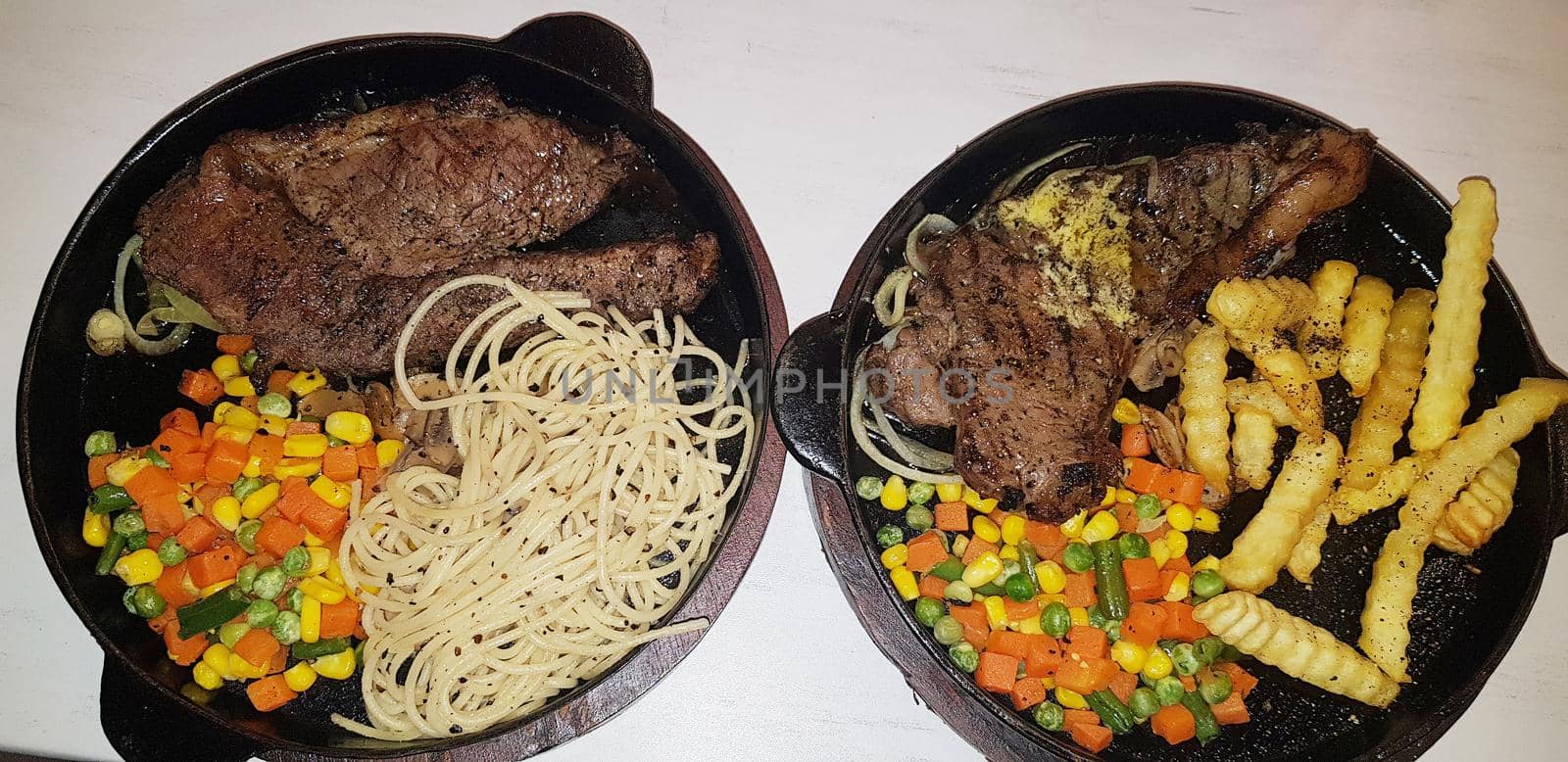 The best food in the world beef steak along with fried potatoes with delicious mushroom sauce and salad and spaghetti plated in beautiful black plate