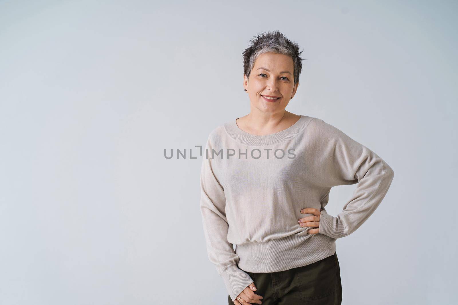 Happy smiling grey hair mature woman 50s posing shoulders slightly up and copy space on right isolated on white background. Copy space and place for product placement. Life care concept by LipikStockMedia