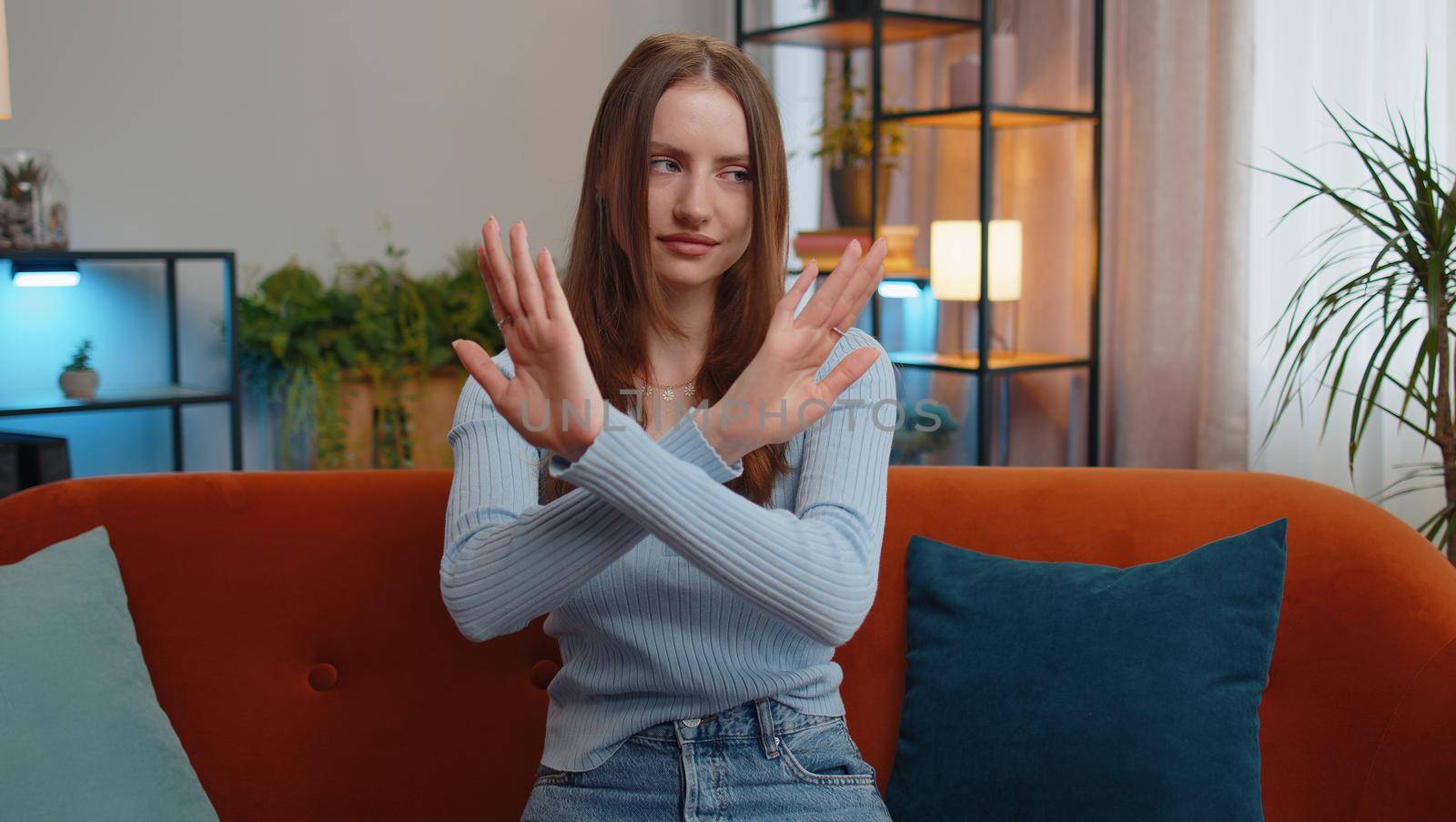 Stop gesture. Angry woman say No hold palm folded crossed hands, warning of finish, prohibited access, declining communication, body language, danger. Girl in home living room sitting on sofa indoors