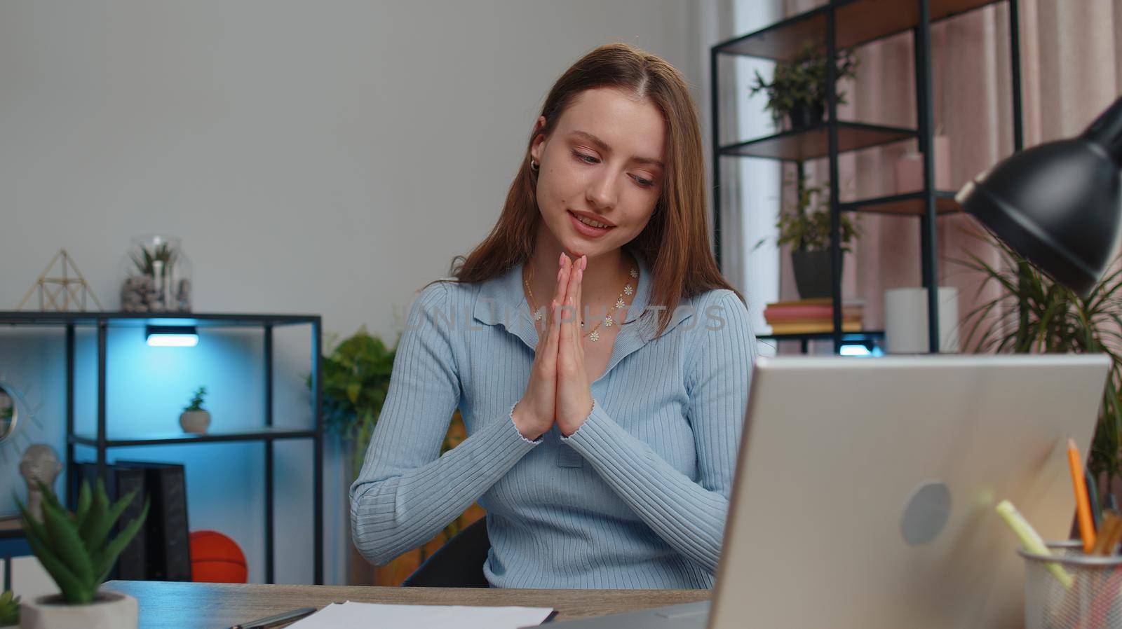 Young woman freelancer sitting at desk at home office pray to God ask for good luck in business, startup, upcoming negotiations. Faith, religion. Girl student study working online remote distance job