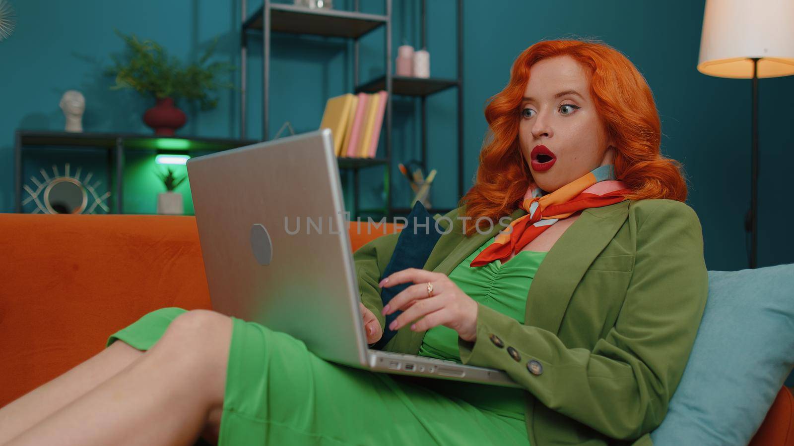 Oh my God Wow. Amazed redhead young woman use laptop computer, receive good news message, shocked by sudden victory, celebrate win, purchases online shopping at home. Ginger girl on living room couch