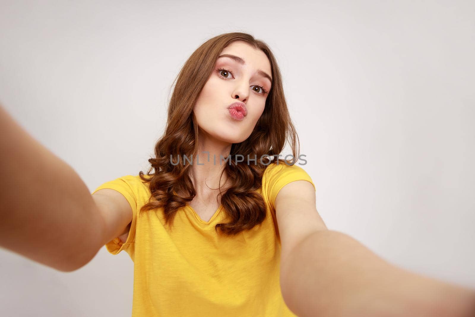 Portrait of lovely teenager girl in yellow casual style t-shirt taking selfie, looking at camera with pout lips POV, sending air kiss. by Khosro1