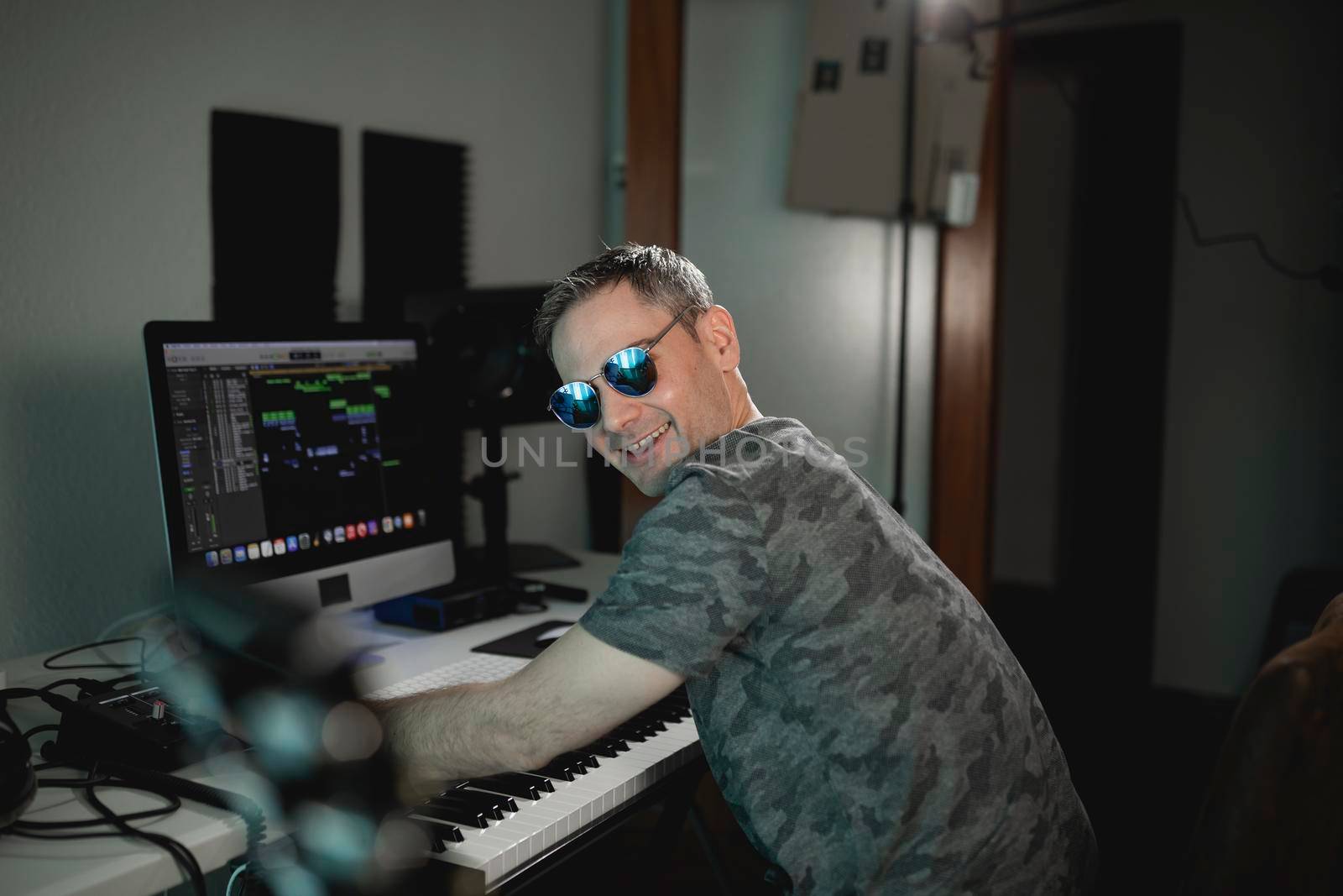 Musician and producer looks at camera smiling with joy while working on a project at his home studio
