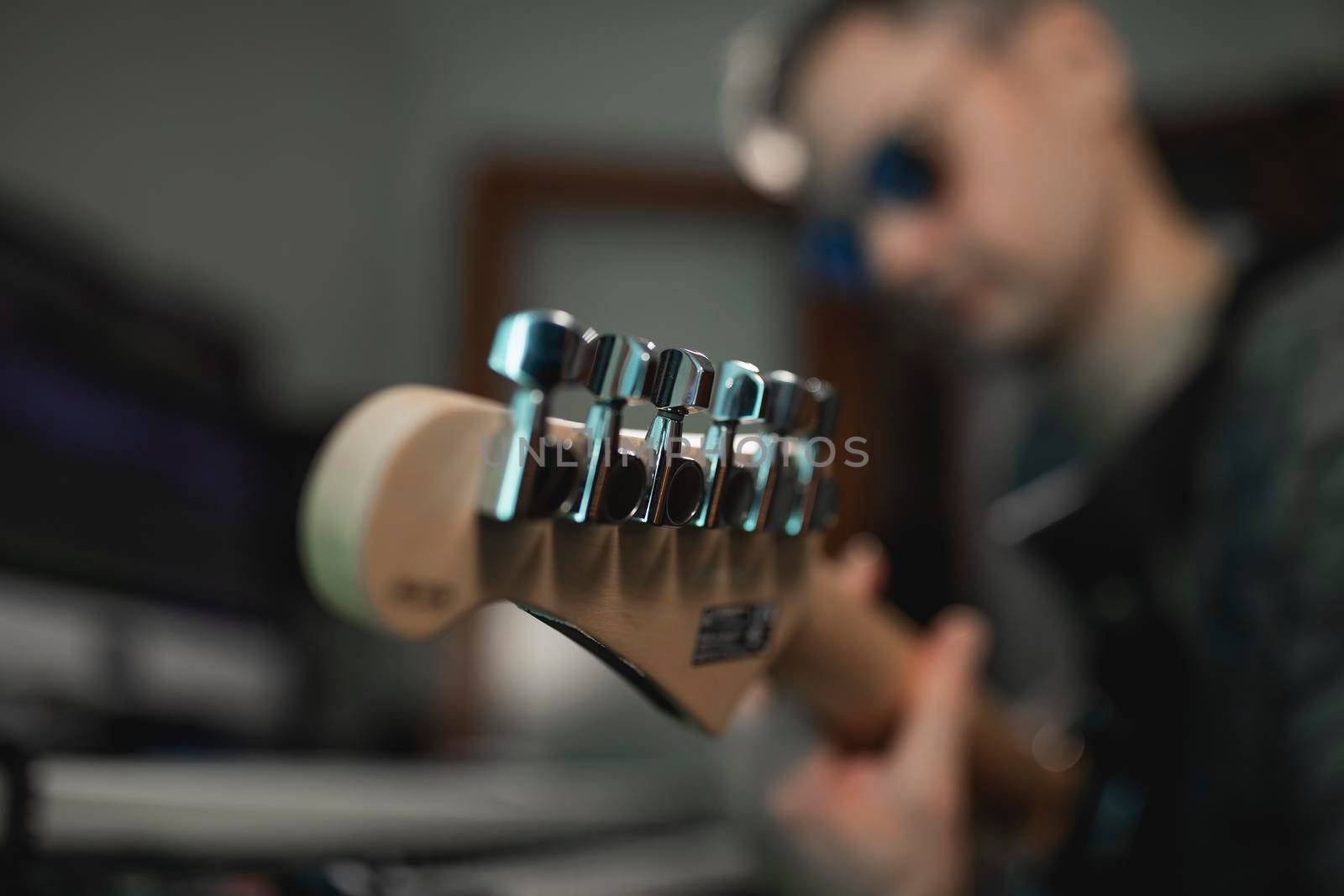 Close-up of the headstock of an electric guitar while being played by a music producer during a recording at his home studio