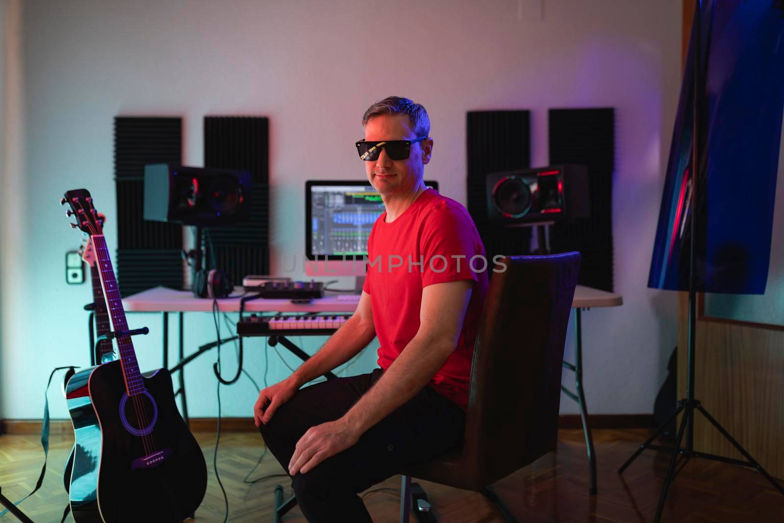 Music producer poses with sunglasses looking at camera while sitting on his chair during a recording session at his home studio