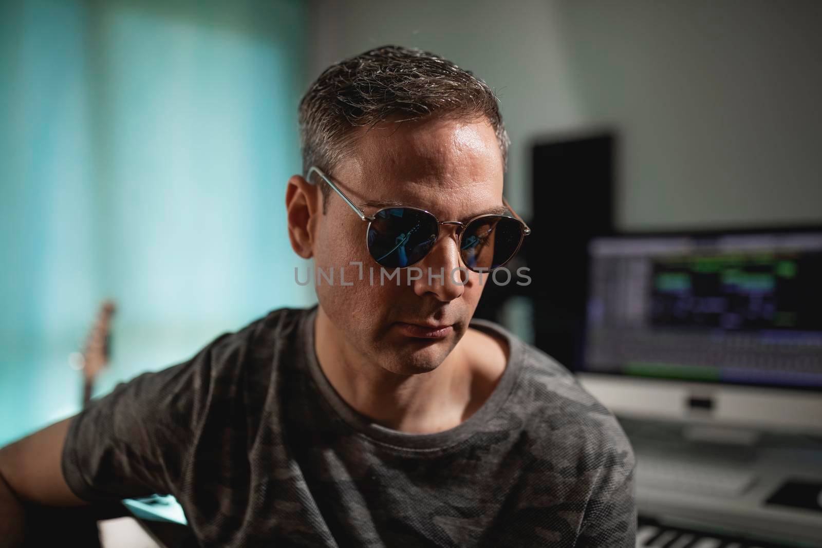 Portrait of a guitarist and producer wearing sunglasses while strumming some chords at his home studio