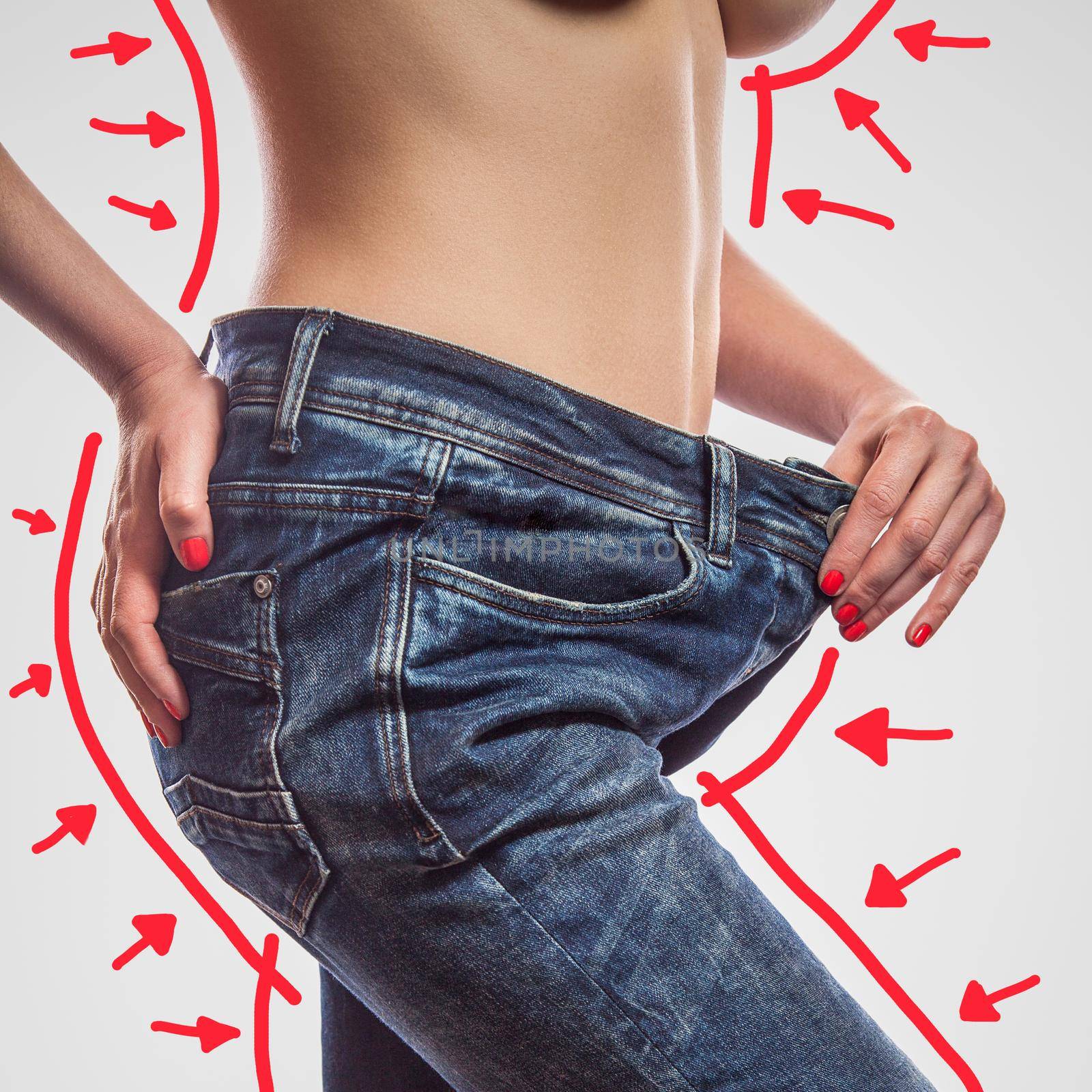 Closeup of slim waist of young woman standing in big jeans showing successful weight loss, indoor studio shot, isolated on light gray background, diet concept.