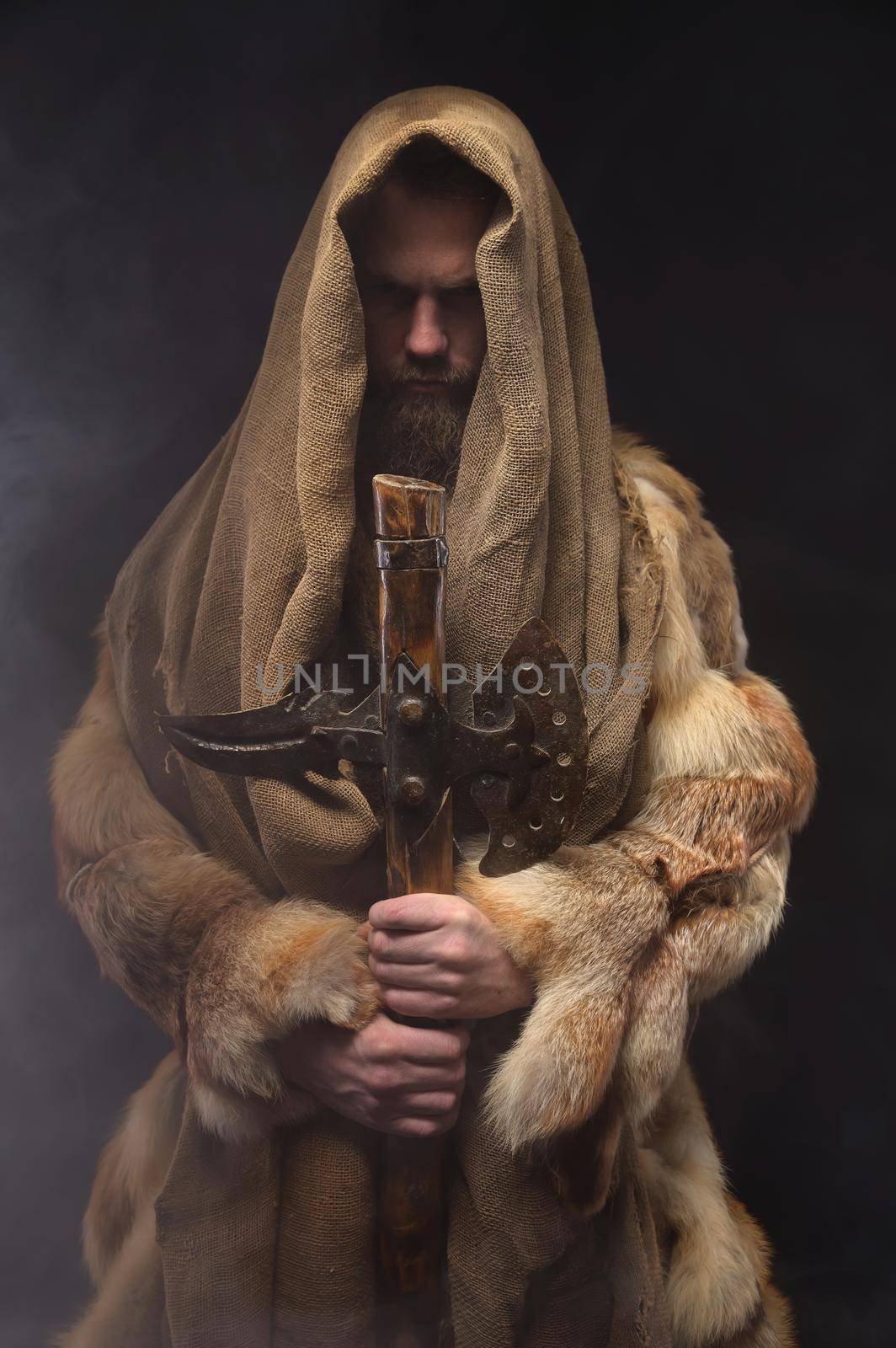 portrait of a brave serious man, a medieval warrior or a monk in a robe, holding an ax, on a dark background. Comparison of eras, history, Renaissance style.