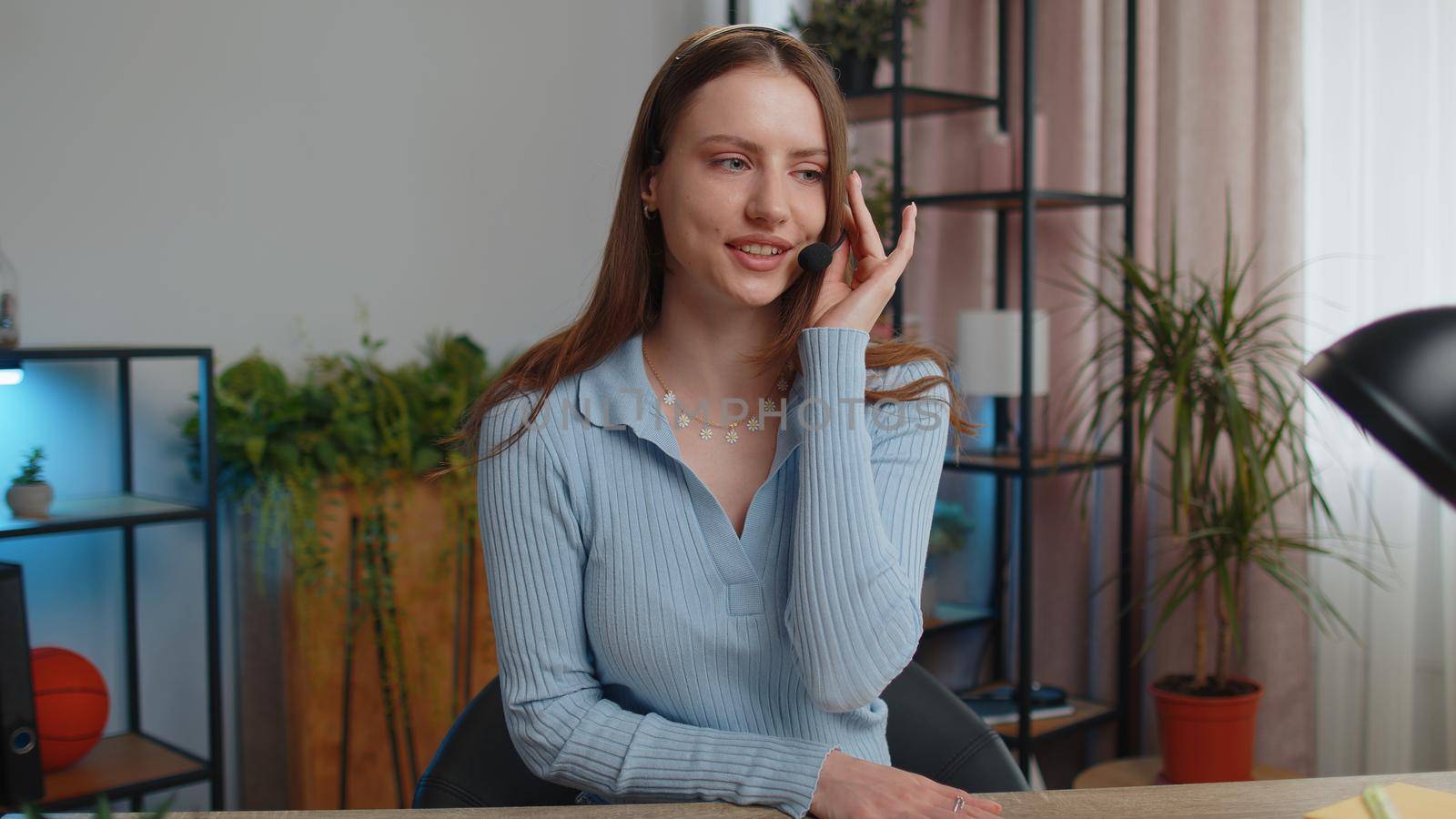 Young business woman sitting at desk at home office wearing headset, freelance worker, call center or support service operator helpline, having talk with client or colleague, communication support