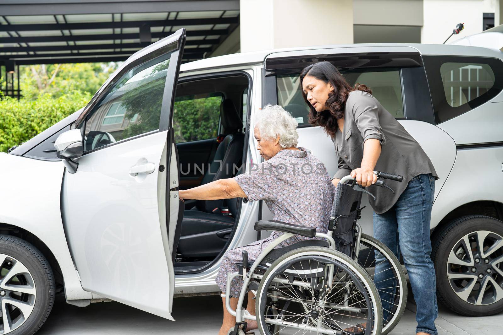 Help and support asian senior or elderly old lady woman patient prepare get to her car. by pamai