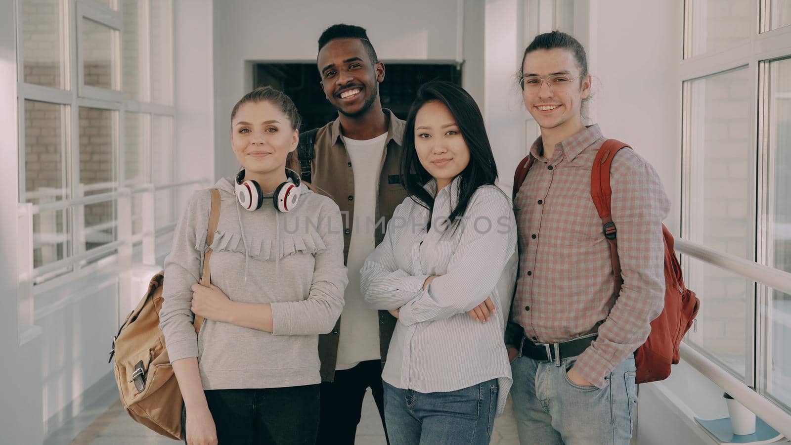 Portrait of four smiling positive attractive multi-ethnic male and female students standing in spacious white corridor in university looking at camera by silverkblack