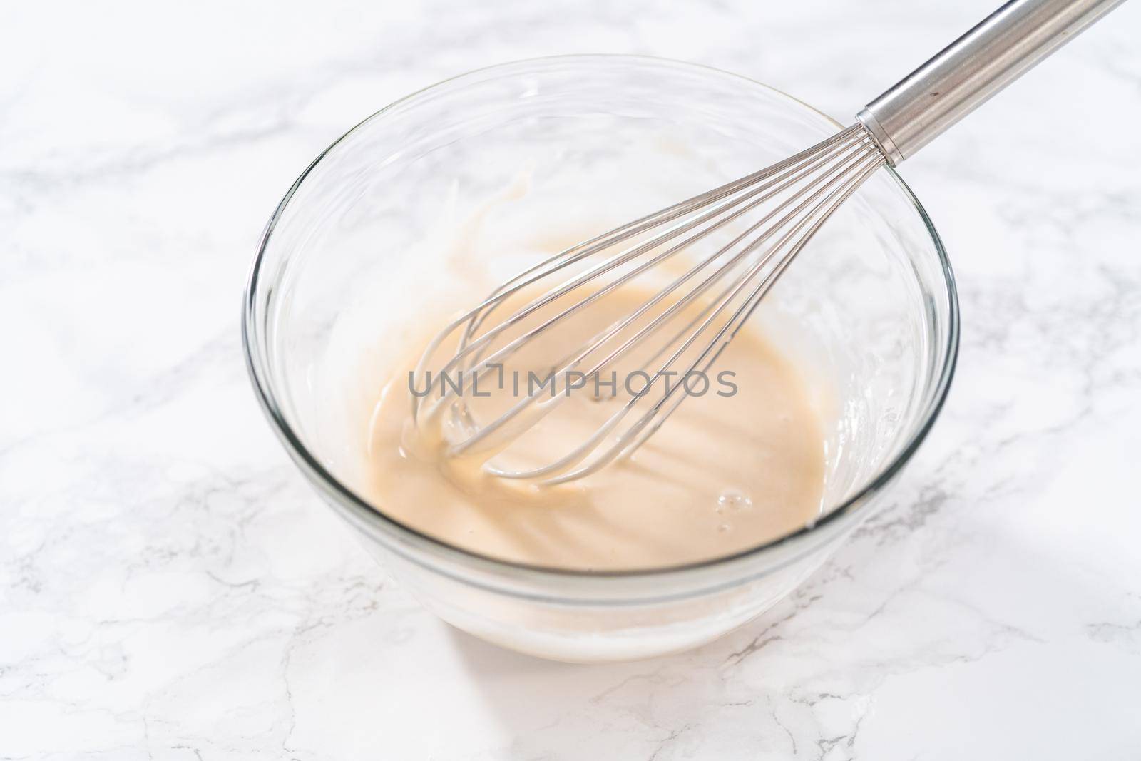 Lemon glaze. Mixing ingredients with a hand whisk in a glass mixing bowl to make lemon glaze.