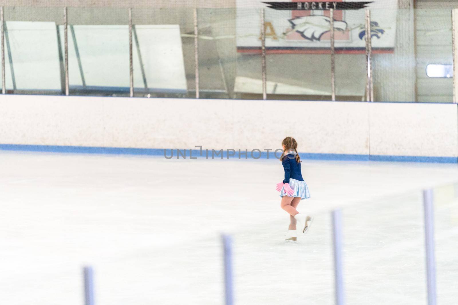 Little girl practicing figure skating on an indoor ice skating rink.