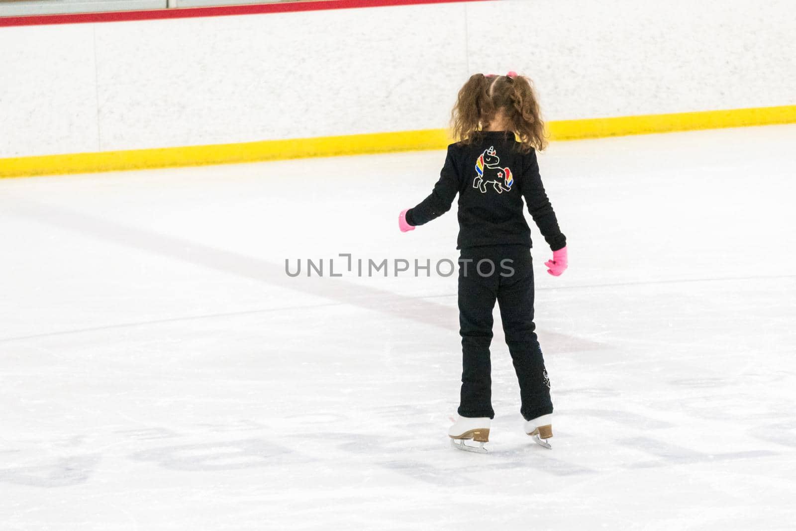 Little girl practicing figure skating moves on the indoor ice rink.