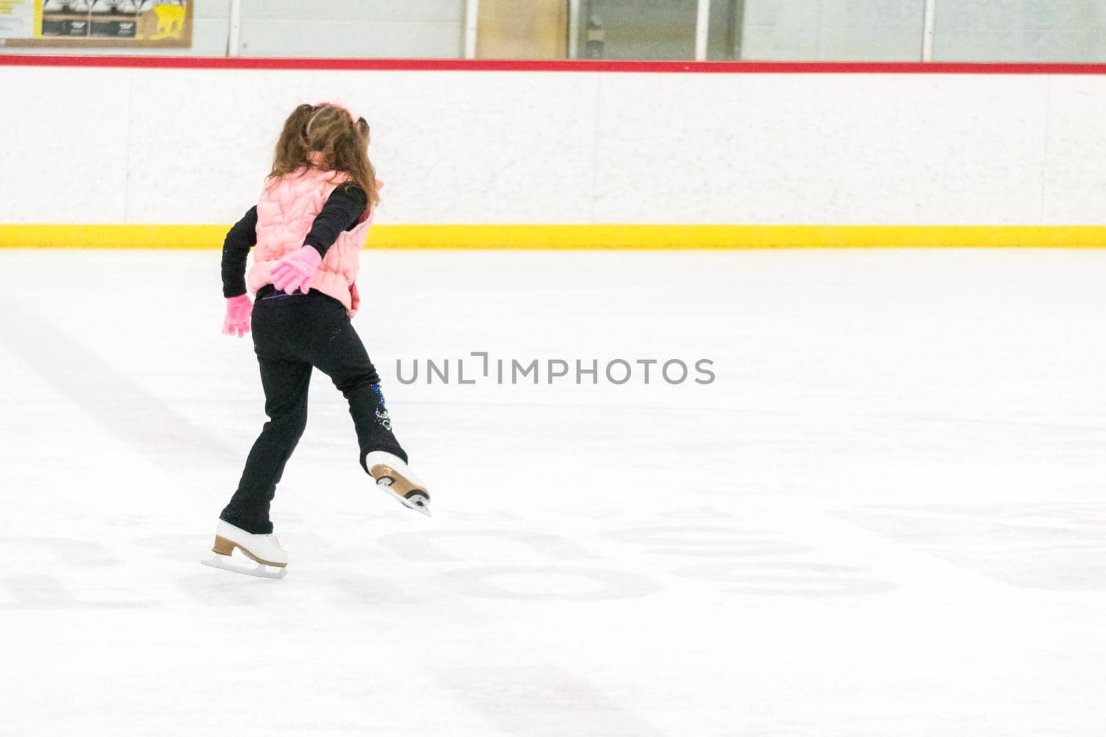 Little girl practicing figure skating moves on the indoor ice rink.