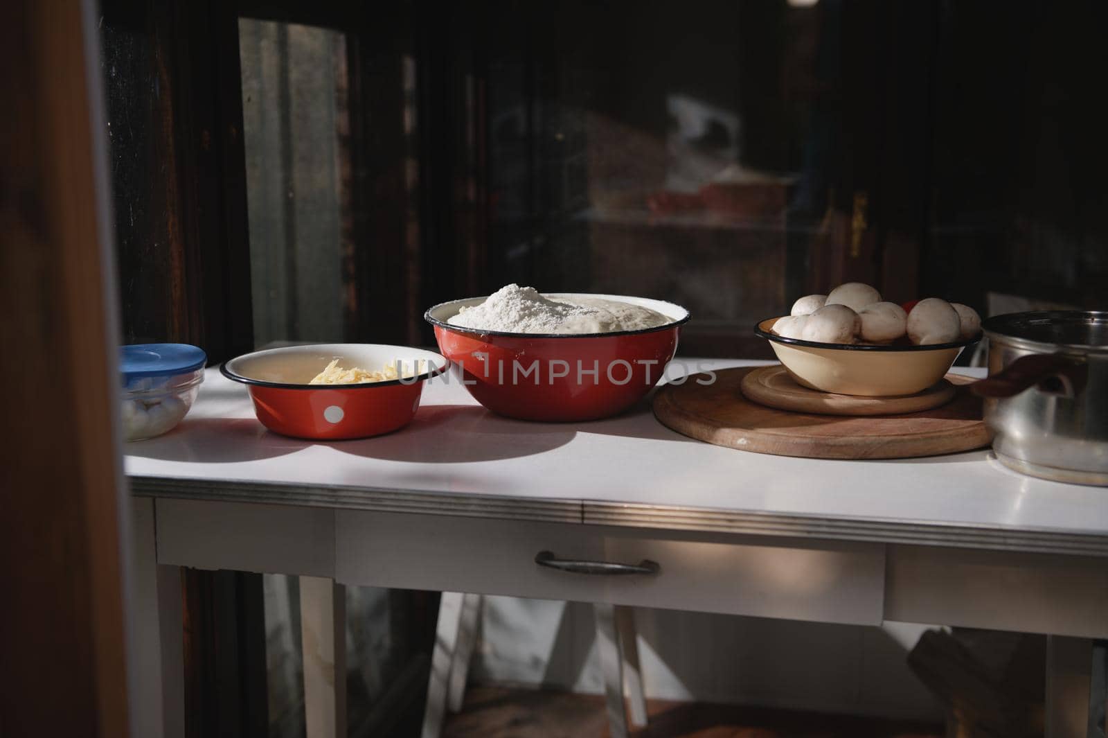 Assortment of fresh pizza ingredients in enamel vintage bowls on a white table in a rustic country house kitchen. Food still life. Raising yeast whole grain dough, fresh vegetables and grated cheese