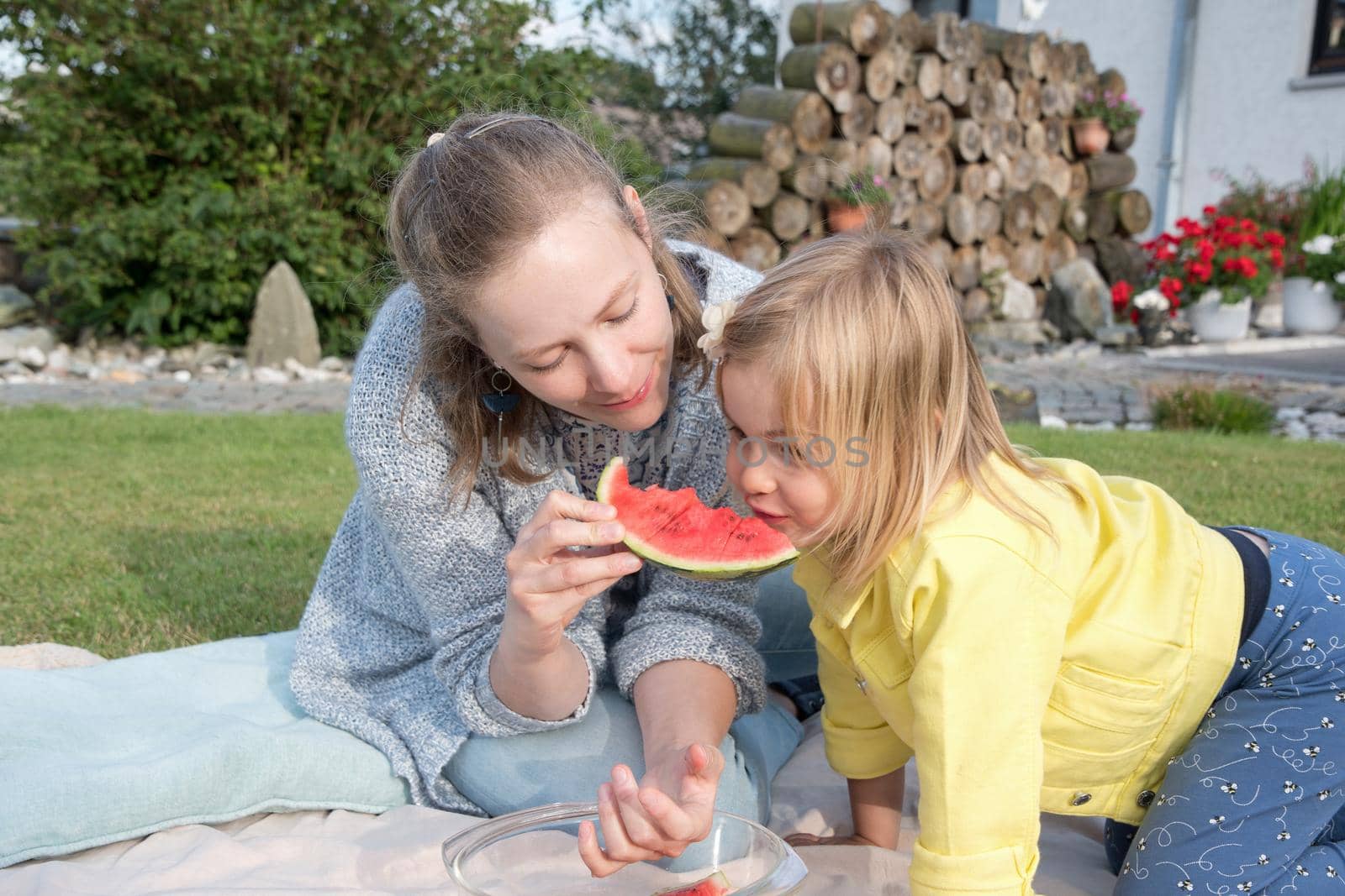 young mother feeds her daughter sweet watermelon, picnic in nature near the house.High quality photo
