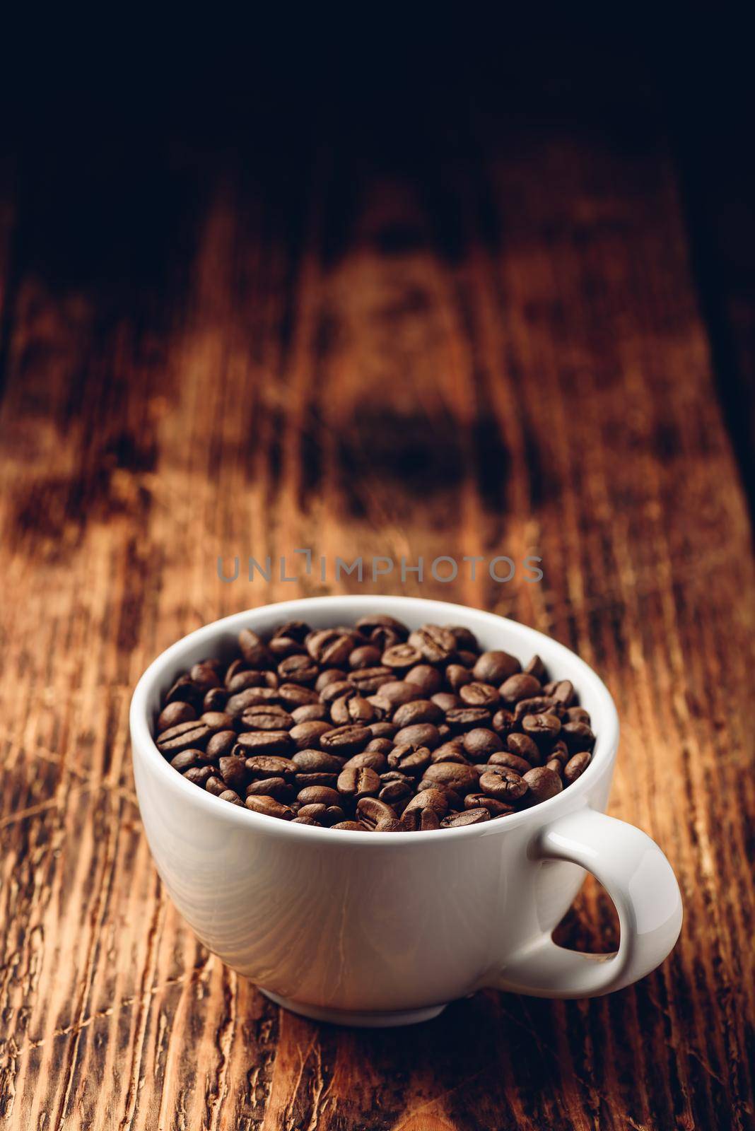 Roasted coffee beans in white cup over rustic wooden surface