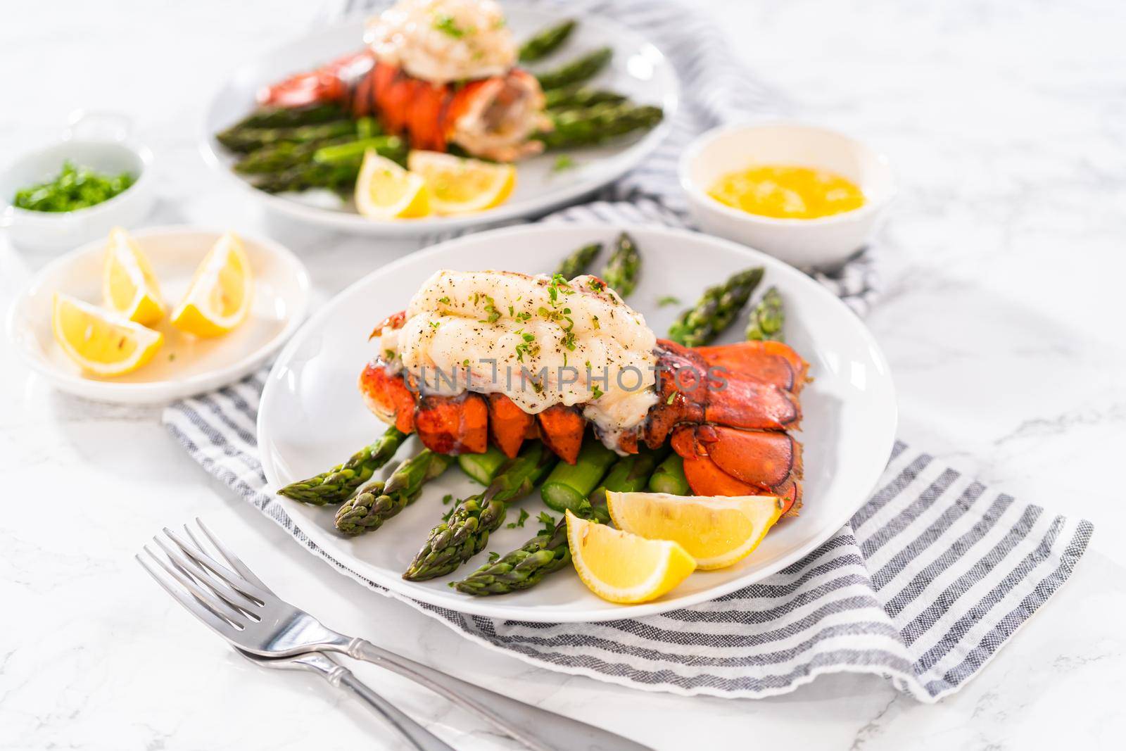 Sering garlic lobster tails with steamed asparagus and lemon wedges on a white plate.