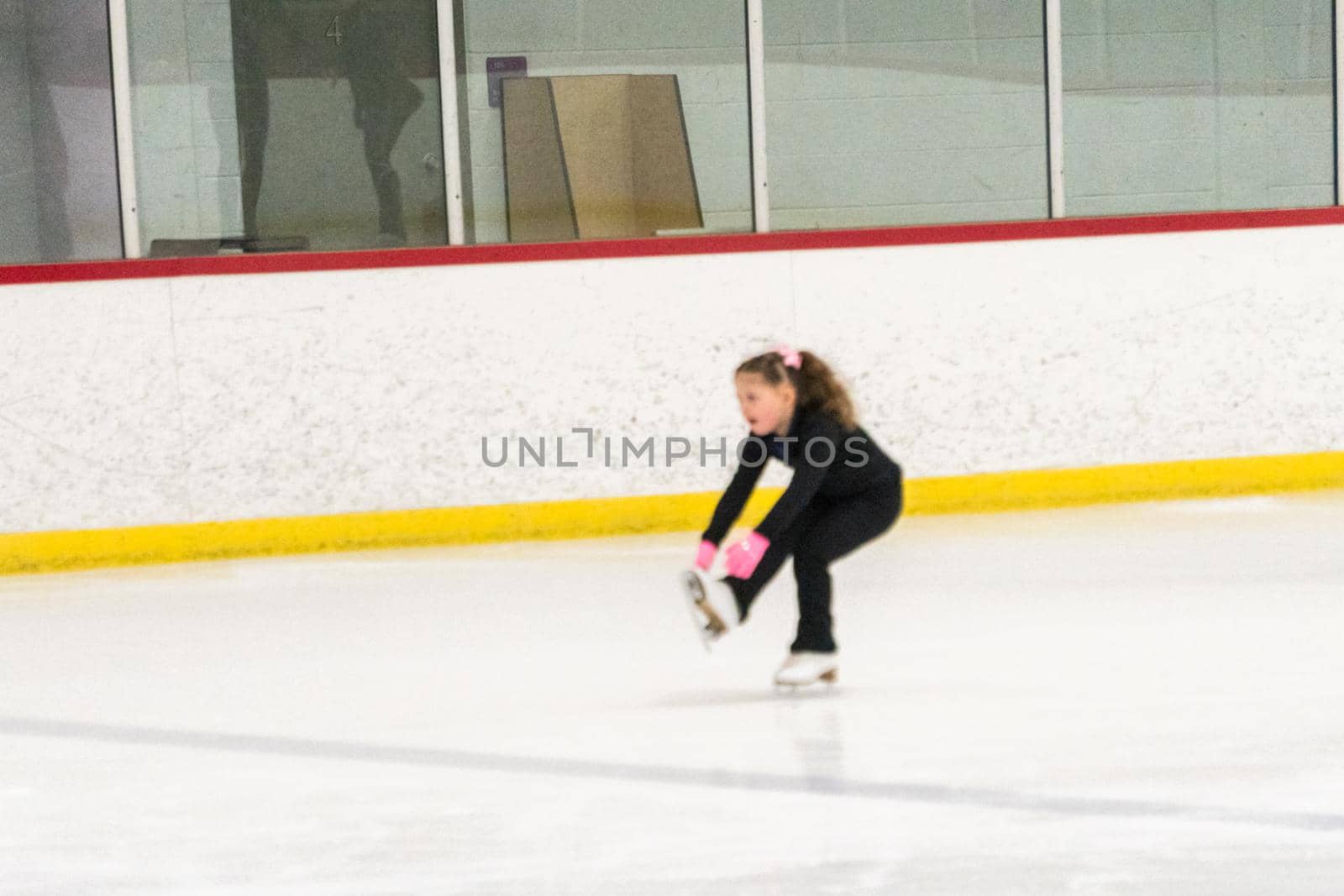 Little girl practicing figure skating moves on the indoor ice rink.