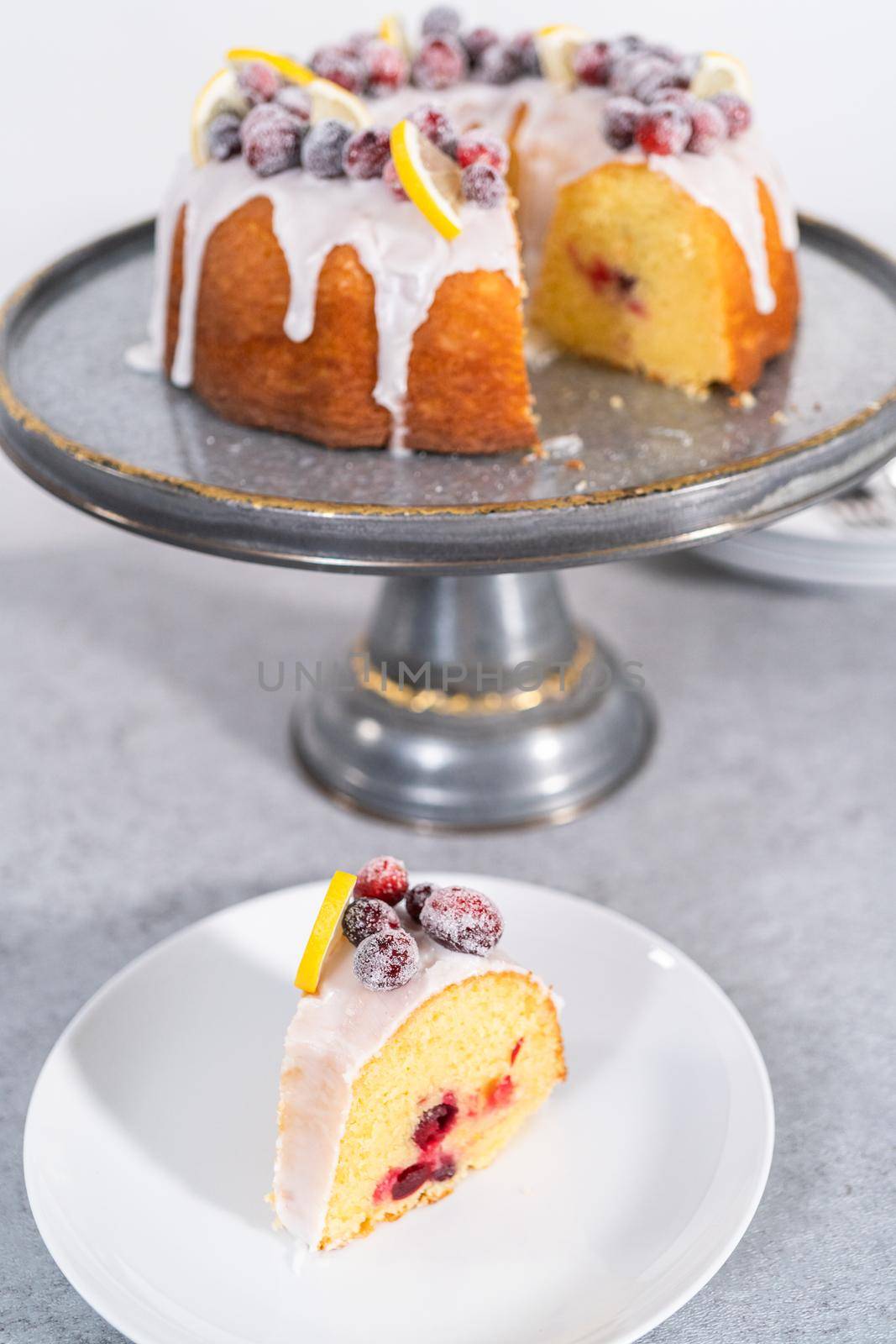 Sliced lemon cranberry bundt cake decorated with sugar cranberries and lemon wedges on a cake stand.