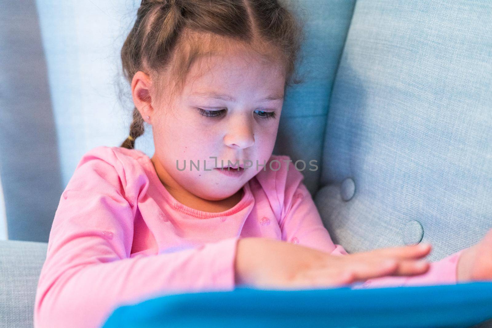 Little girl reading books on her tablet at homeschool.