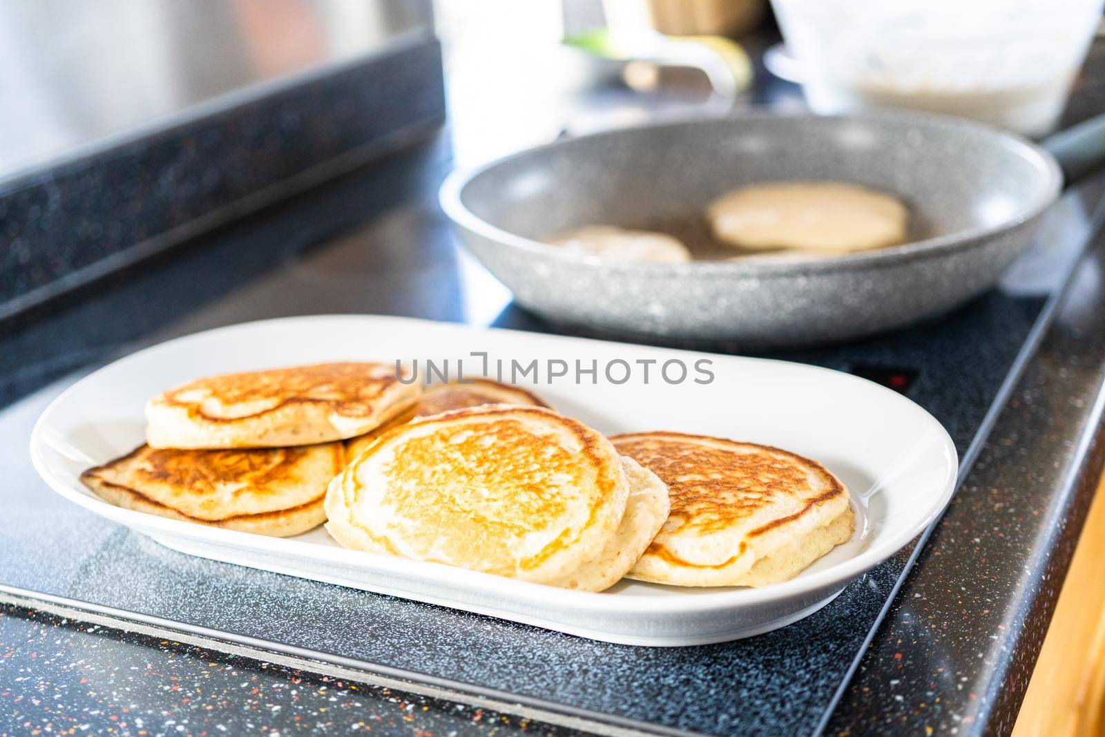 Frying kefir based pancakes in cooking pan on an electric stove.