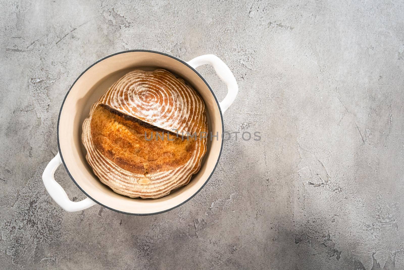 Flat lay. Freshly baked loaf of a wheat sourdough bread with marks from bread proofing basket in enameled cast iron dutch oven.