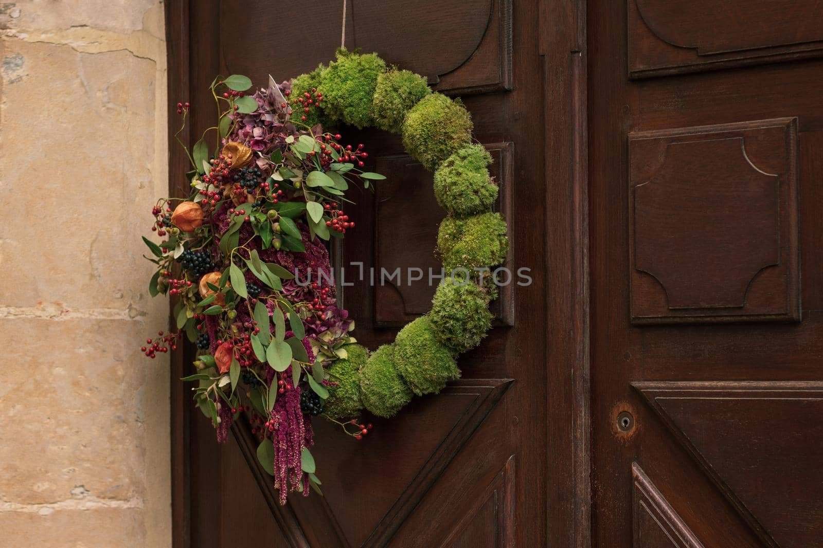 Wreath with the red berries and the dry leaves and fruits hanging on a door.