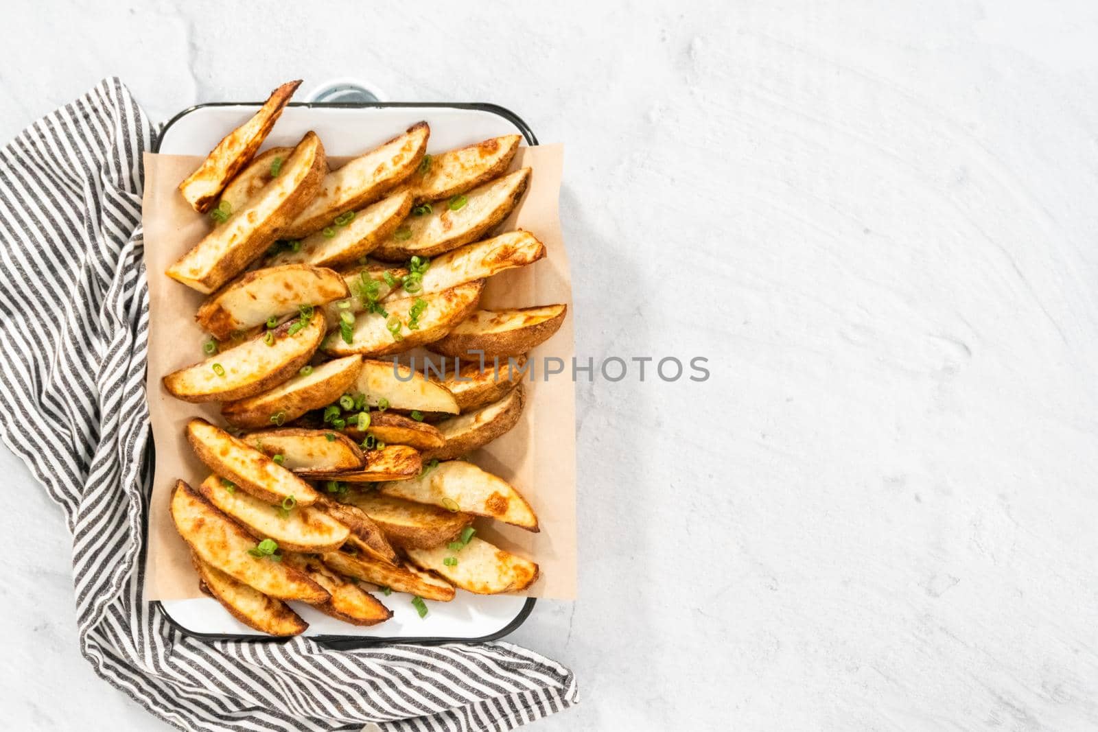 Flat lay. Freshly baked potato wedges with spices on a white serving tray.